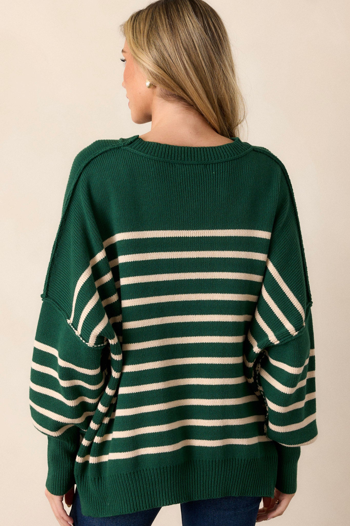 Back view of a green stripe sweater highlighting the overall fit, ribbed hem with side slits, and horizontal stripe pattern.