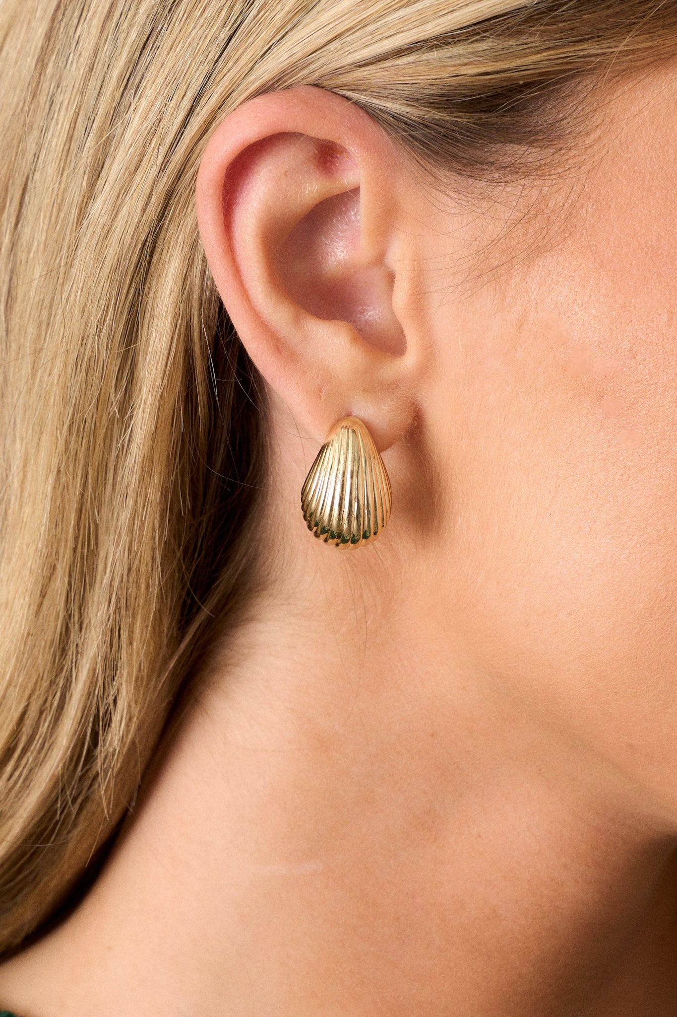 Close up view of these gold earrings that  feature gold finish, a teardrop shape, a ripple texture, and secure post hole backings.