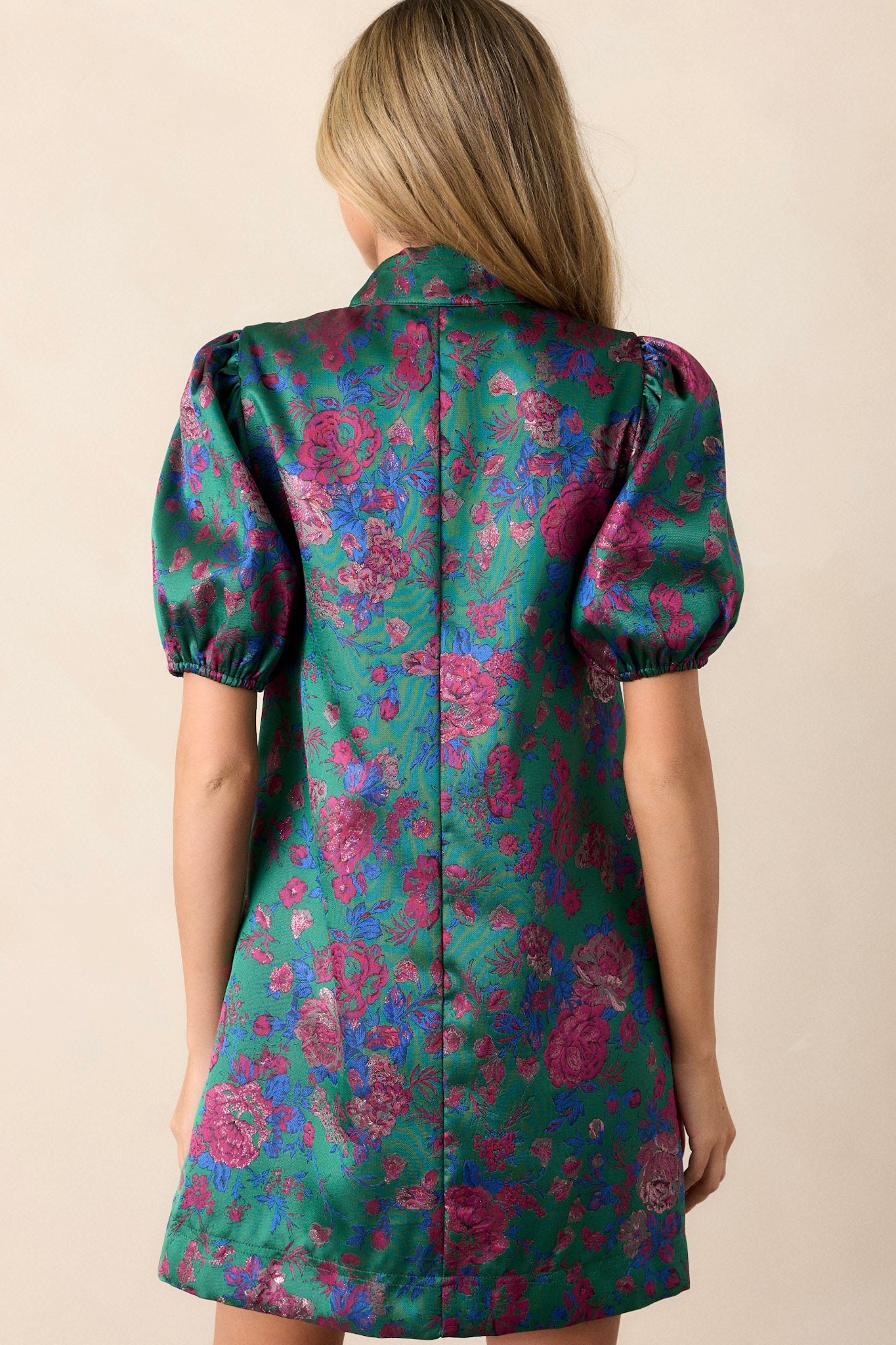 Back  view of this green dress that features a tie-neckline, elastic puff sleeves, multi-color jacquard fabric, and a mini length.