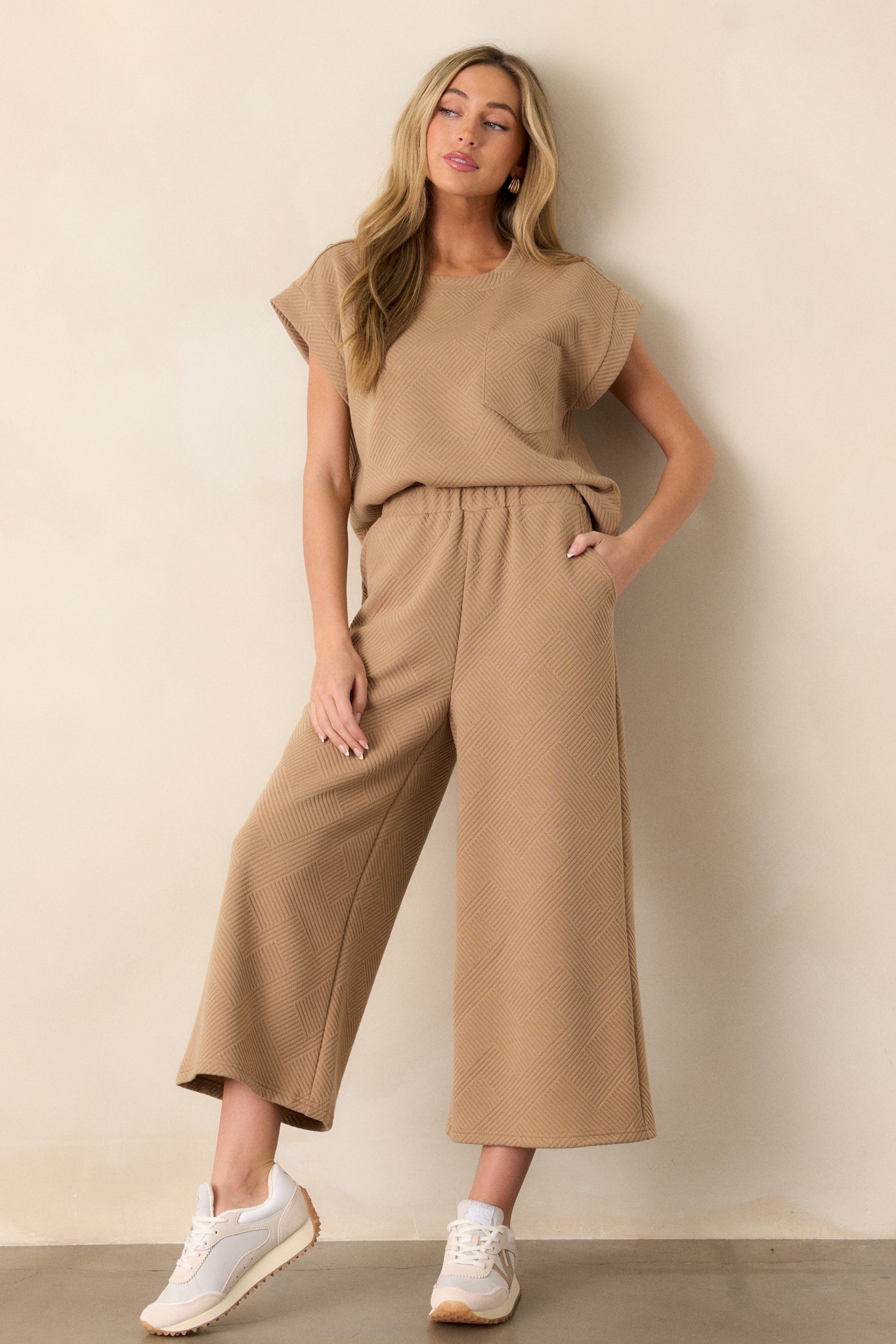 Tan pants showcasing a high-waisted fit, elastic waistband, hip pockets, textured crisscross pattern, and wide-leg design.