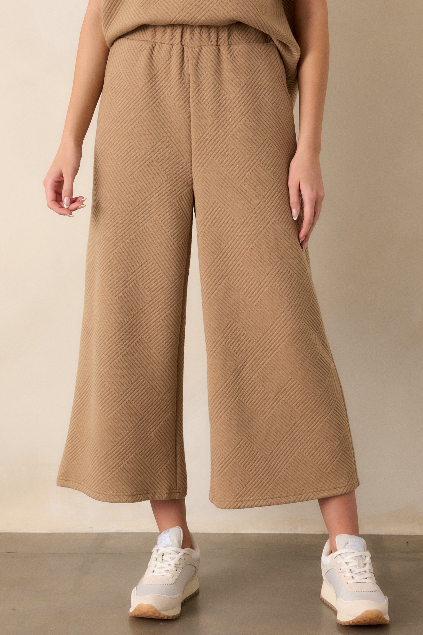 Close-up of tan pants highlighting the textured crisscross pattern, elastic waistband, and functional hip pockets with a wide-leg cut.