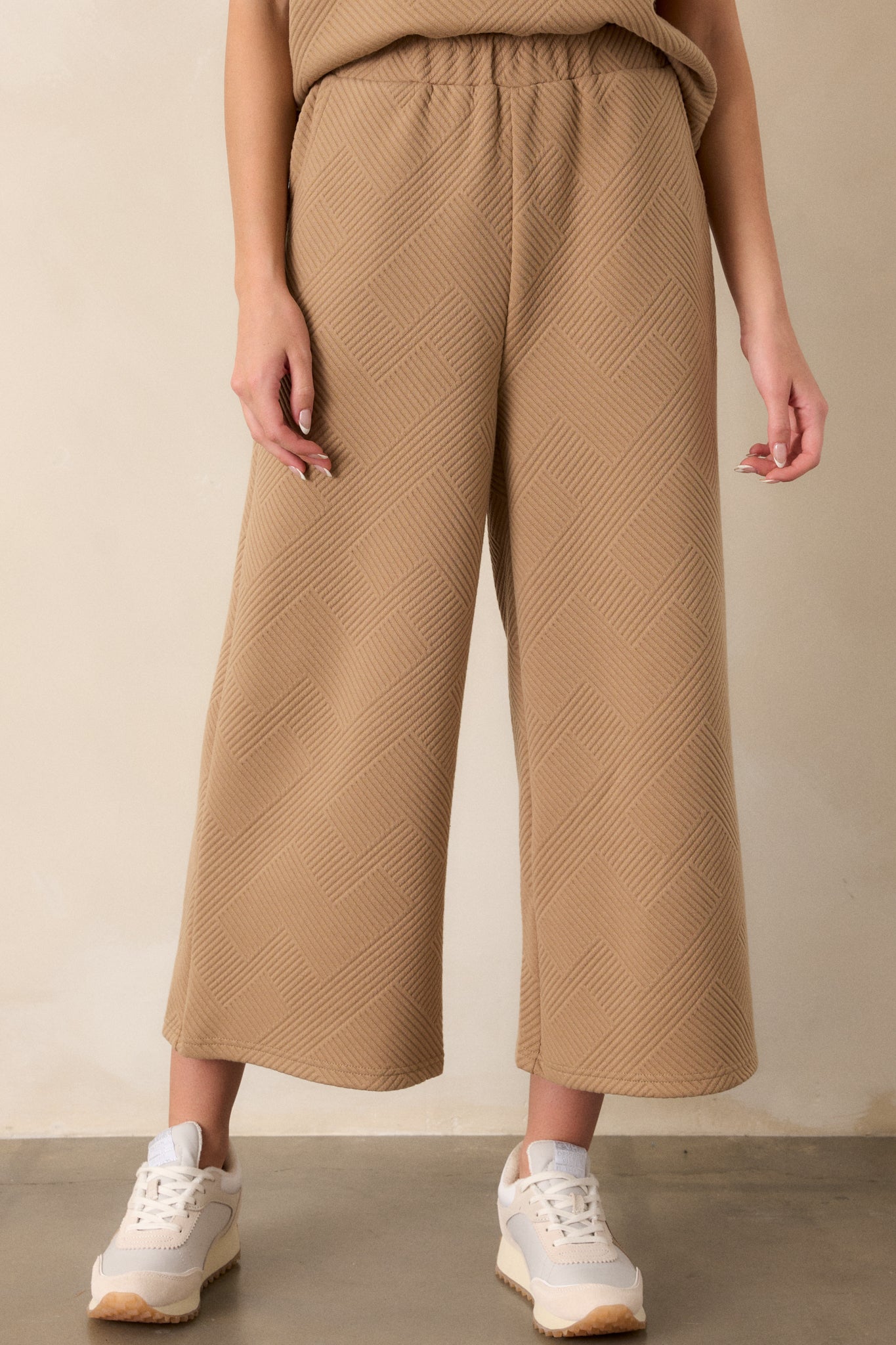 Detailed view of tan pants emphasizing the high-waisted design, textured crisscross pattern, elastic waistband, and wide-leg fit.