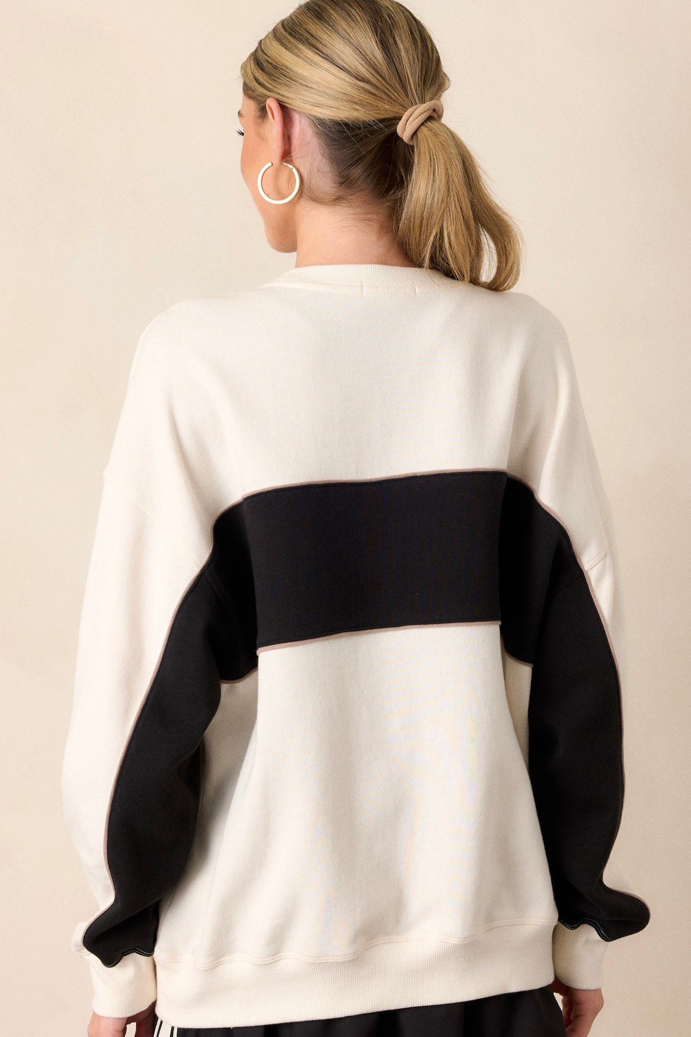 A view of the back of the ivory sweatshirt, emphasizing the simplicity of the design while showcasing the ribbed hemline and overall fit.