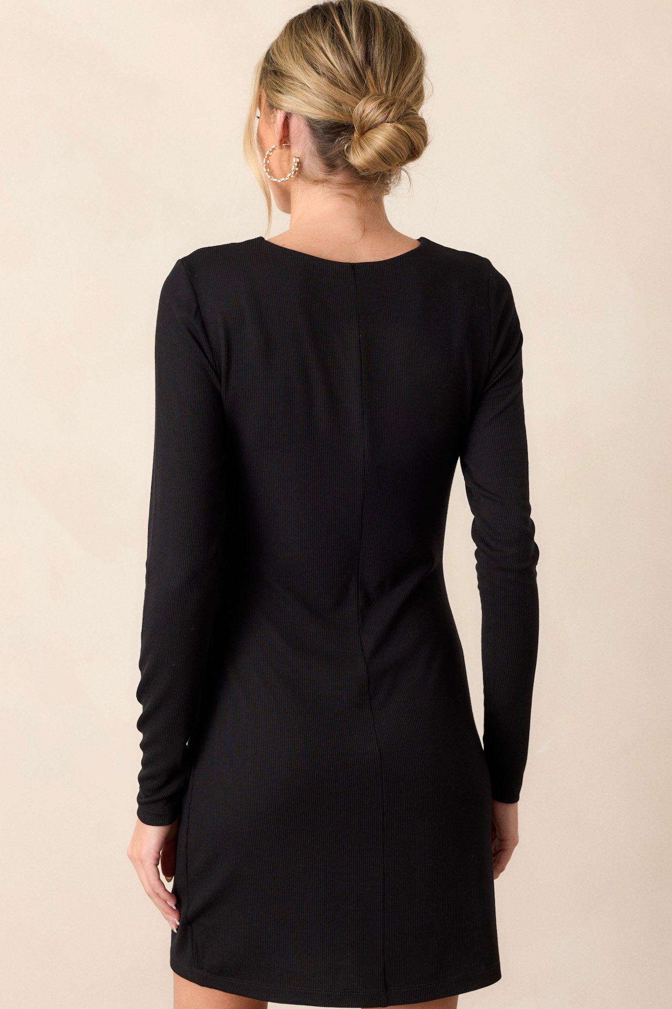 A view of the back of the black mini dress, highlighting the crew neckline and the fitted ribbed bodice, with long sleeves continuing down the arms.