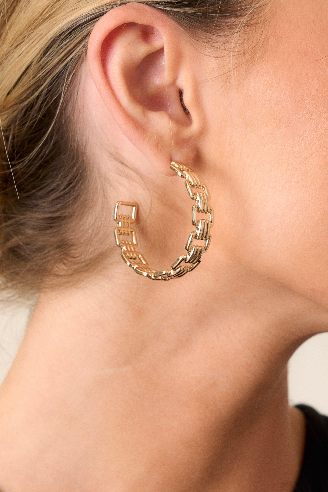 Close-up view of these gold hoop earrings featuring an incomplete hoop design, square shaped links, and secure post backings.