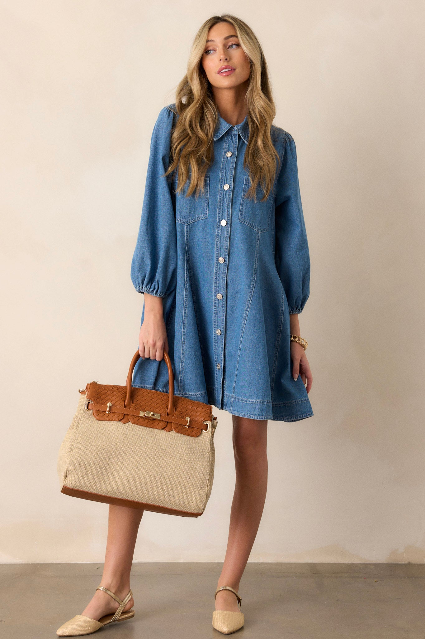 This medium wash denim dress features a collared neckline, a functional button front, functional chest pockets, functional hip pockets, a relaxed fit and elastic cuffed three-fourth sleeves.