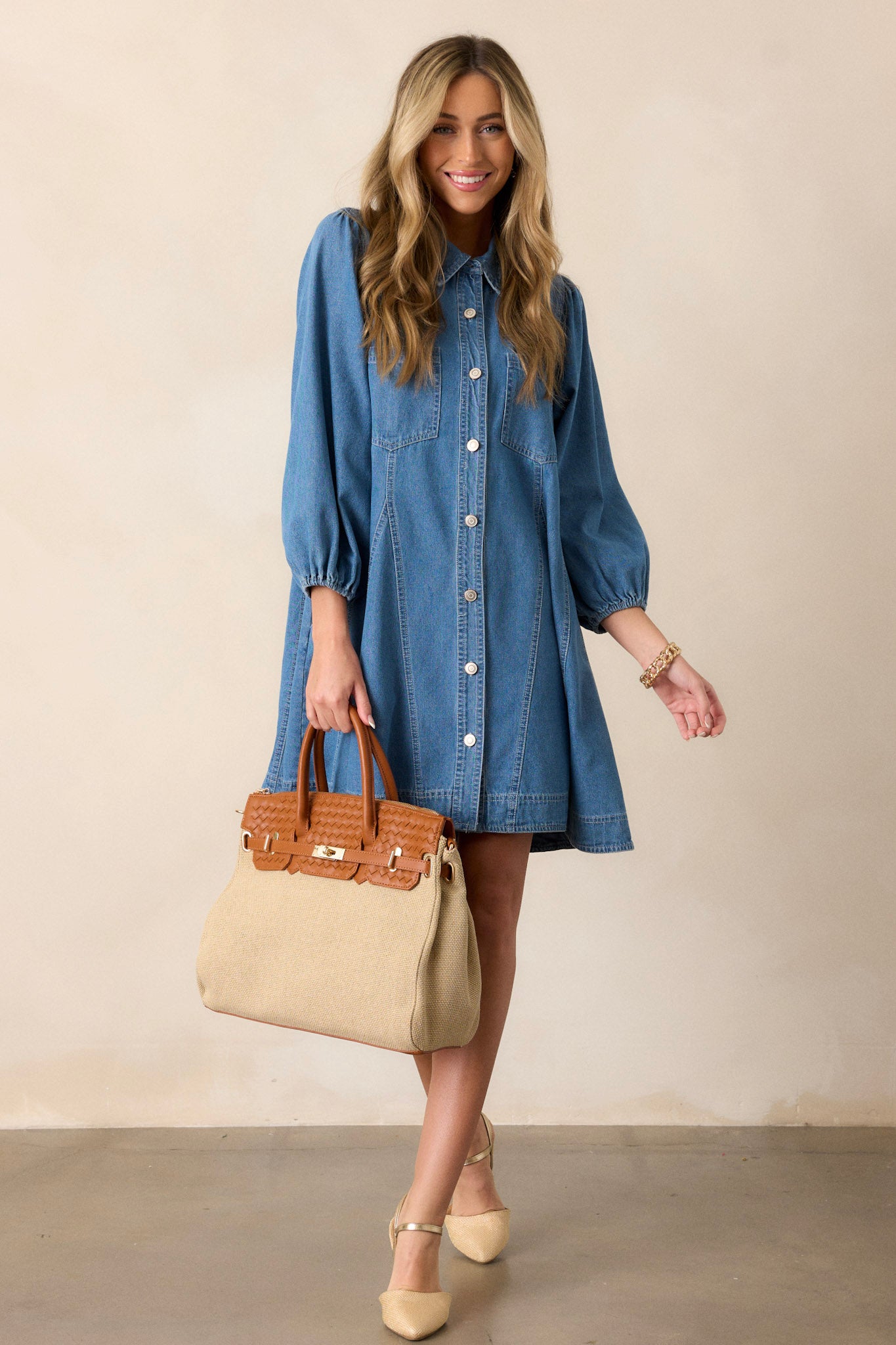 Full body view of this medium wash denim dress that features a collared neckline, a functional button front, functional chest pockets, functional hip pockets, a relaxed fit and elastic cuffed three-fourth sleeves.