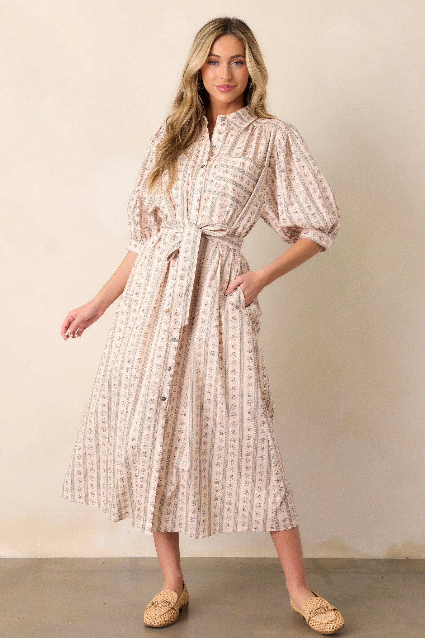 Full body view of this ivory dress 
that features a functional button front, a tie belt, puff button sleeves, and a popped collar.