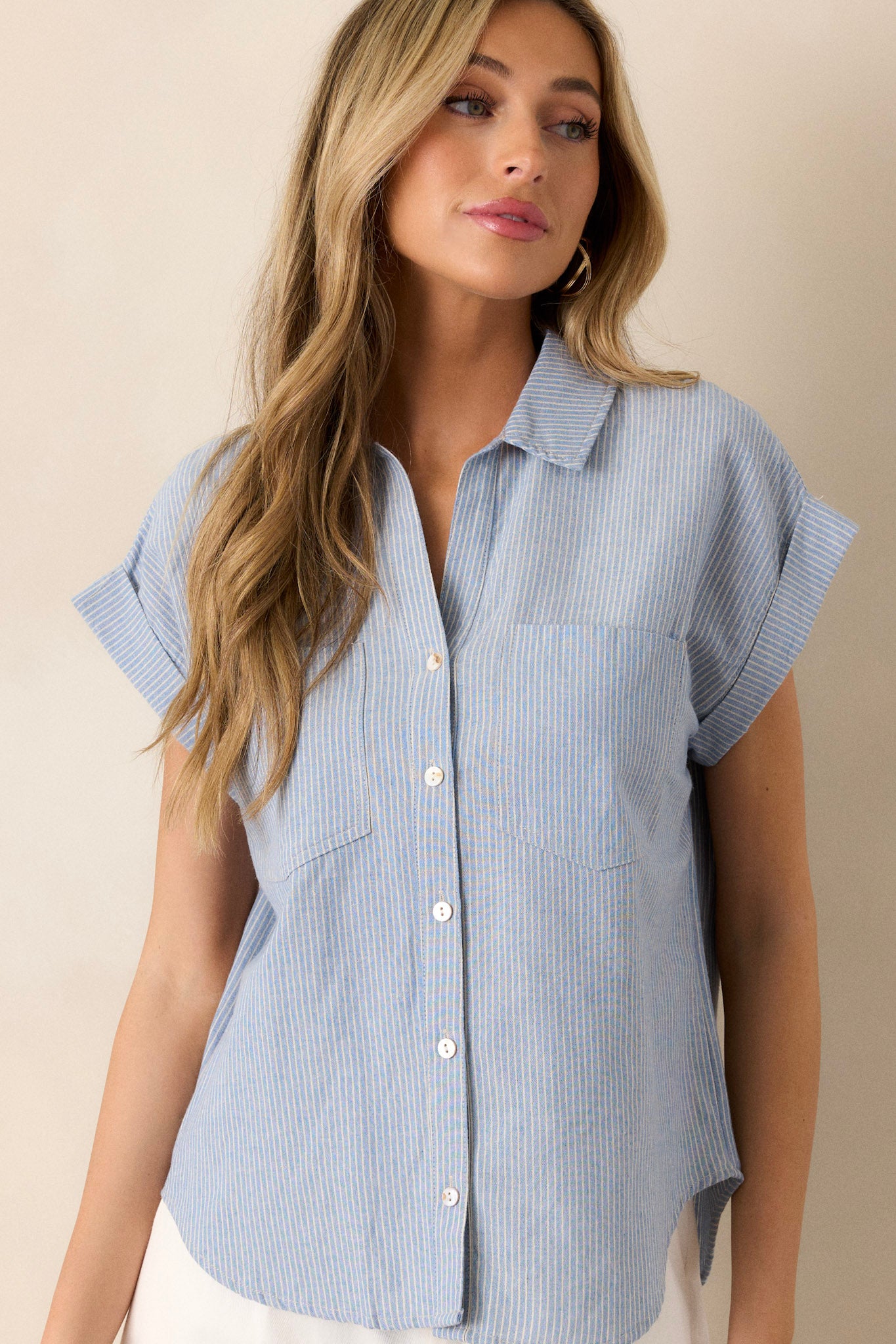 Front angled view of this light blue stripe top that features a collared v-neckline, a functional button front, a vertical stripe pattern, functional bust pockets, and cuffed short sleeves.