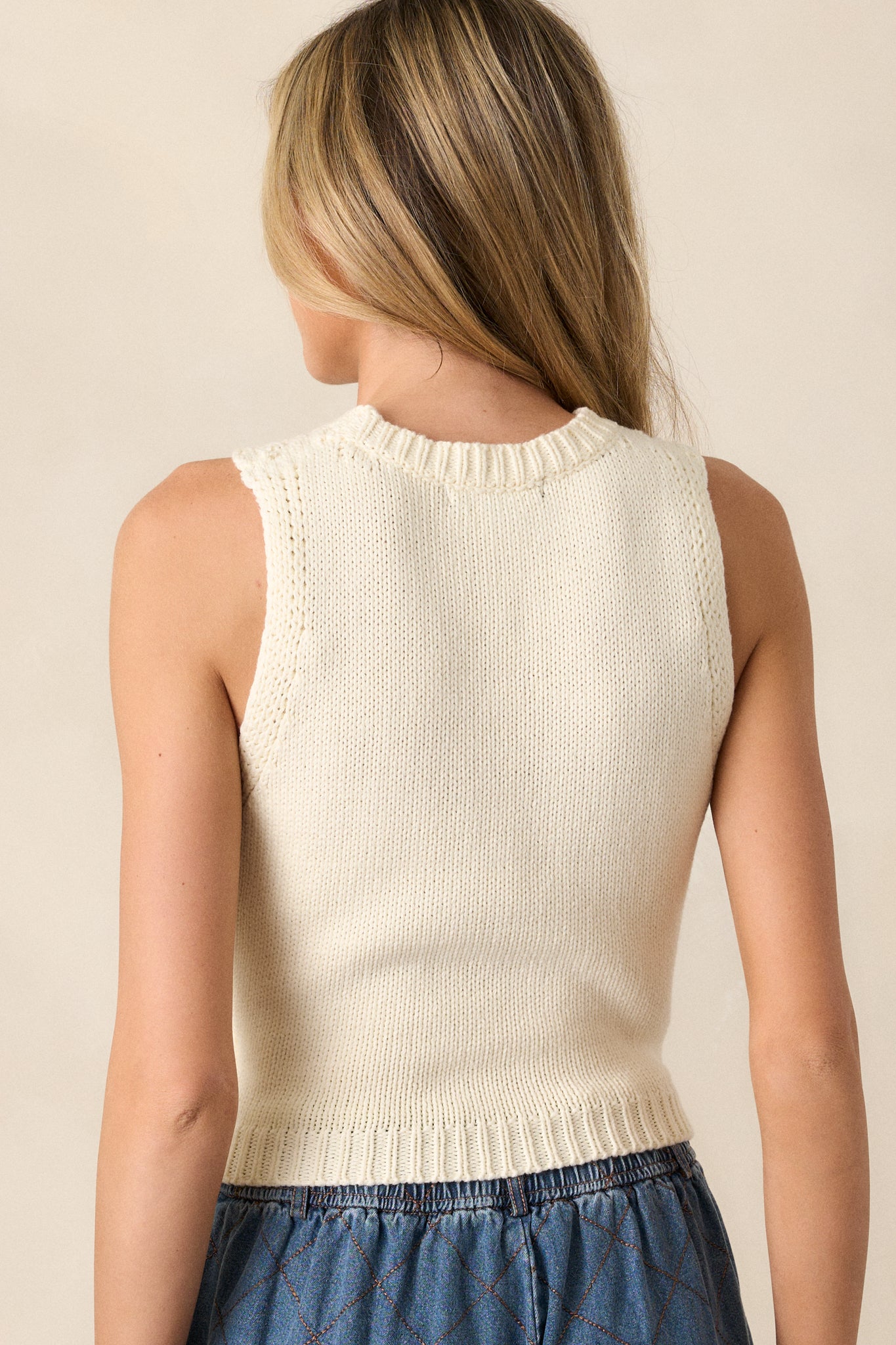 A back view of the ivory vest, showcasing the knitted texture and ribbed neckline and waistline from the rear.