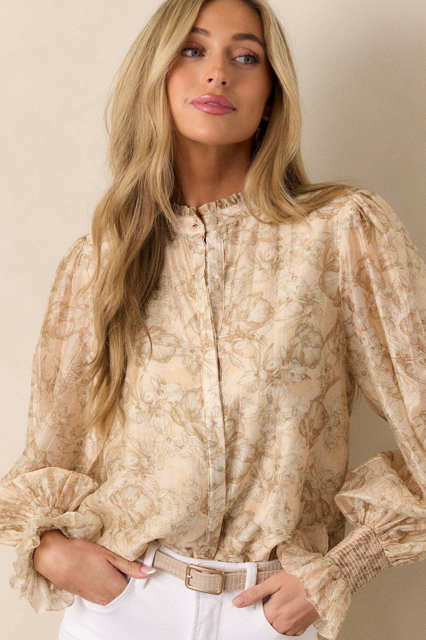 Close-up view of the beige top’s upper section, focusing on the high pleated ruffle neckline and floral design.