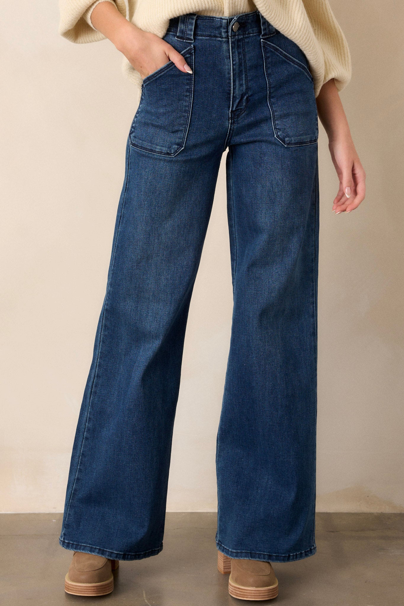 Close up view of these dark wash jeans featuring a high waisted design, classic button zipper closure, belt loops, functional front patch pockets, and a flare leg.