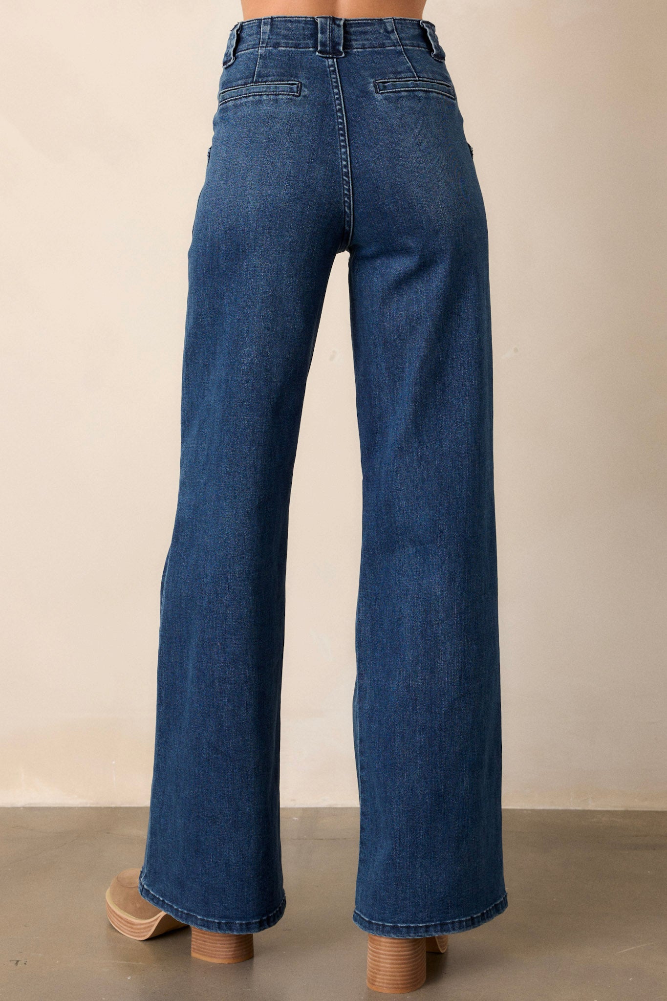 Back view of these dark wash jeans featuring a high waisted design, classic button zipper closure, belt loops, functional front patch pockets, and a flare leg.