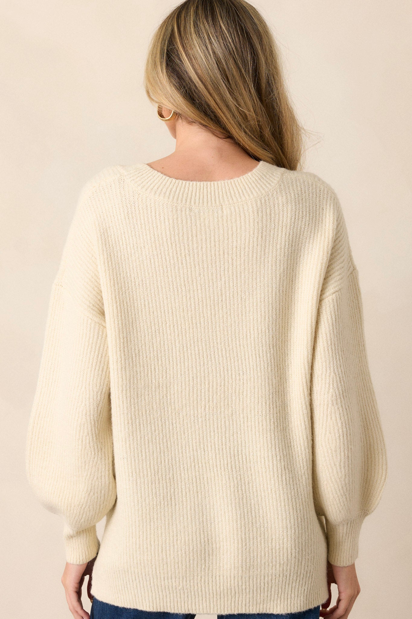 Back view of this sweater that features a v-neckline, long sleeves with ribbed cuffs, a ribbed hemline, and slits that go up each side with the back being slightly longer.