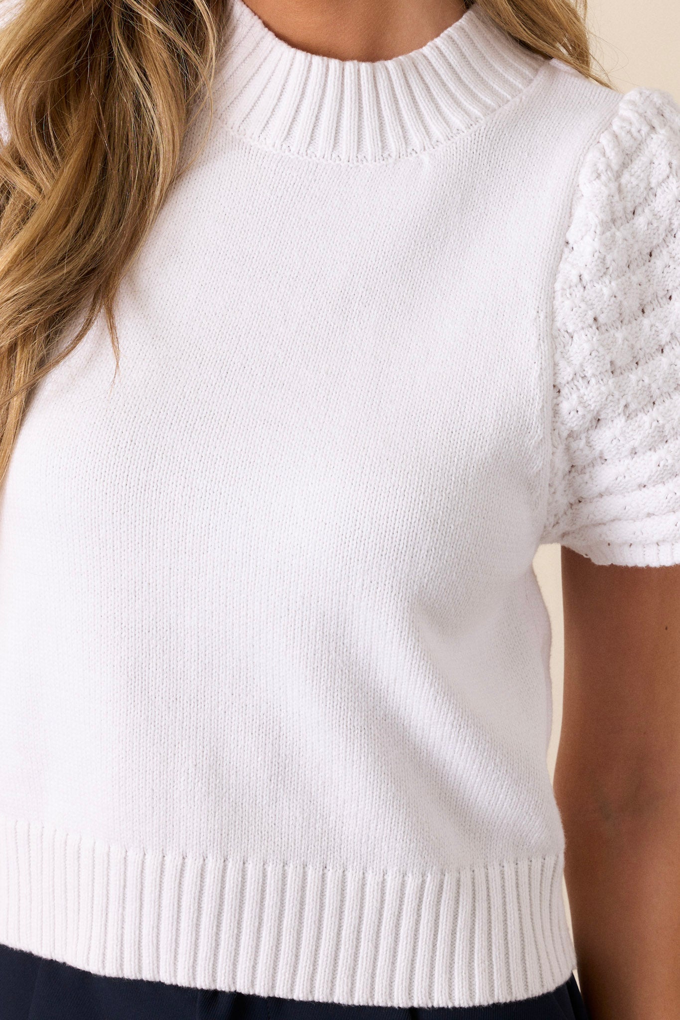 Close-up of a white short sleeve sweater showing the ribbed collar and the texture of the cap sleeves.