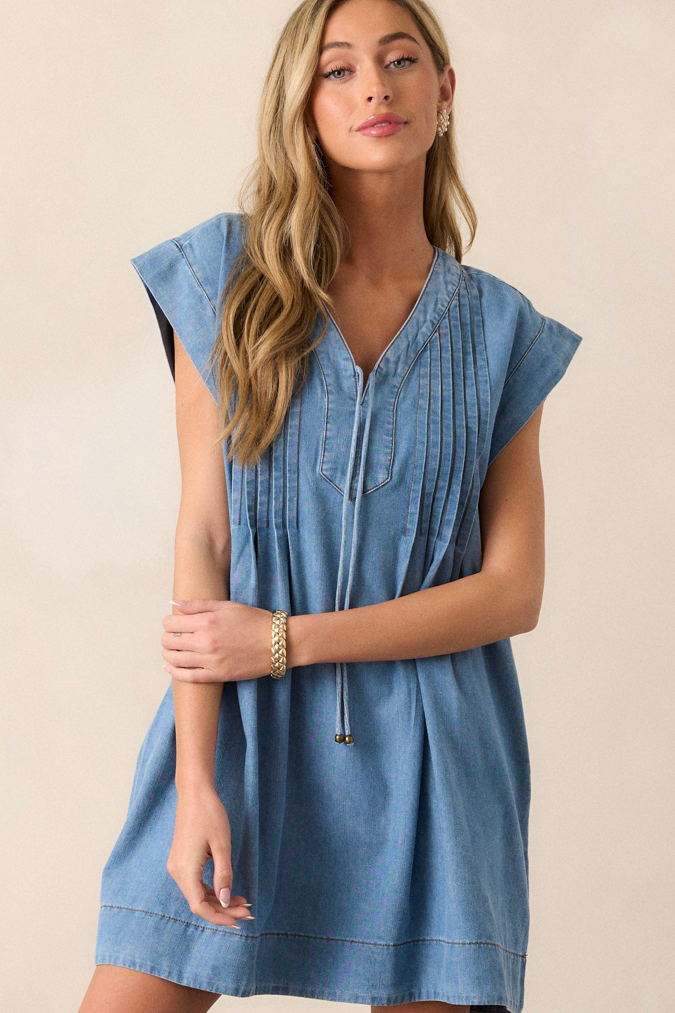 This chambray dress features a v-neckline, a self-tie feature, functional pockets, and pin tuck pleating around neckline.