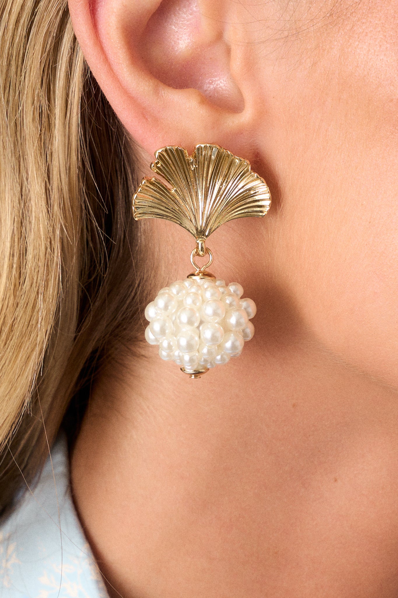 Close-up view of these earrings that feature gold hardware, a textured leaf stud, a pearl cluster drop, and secure post hole backings.