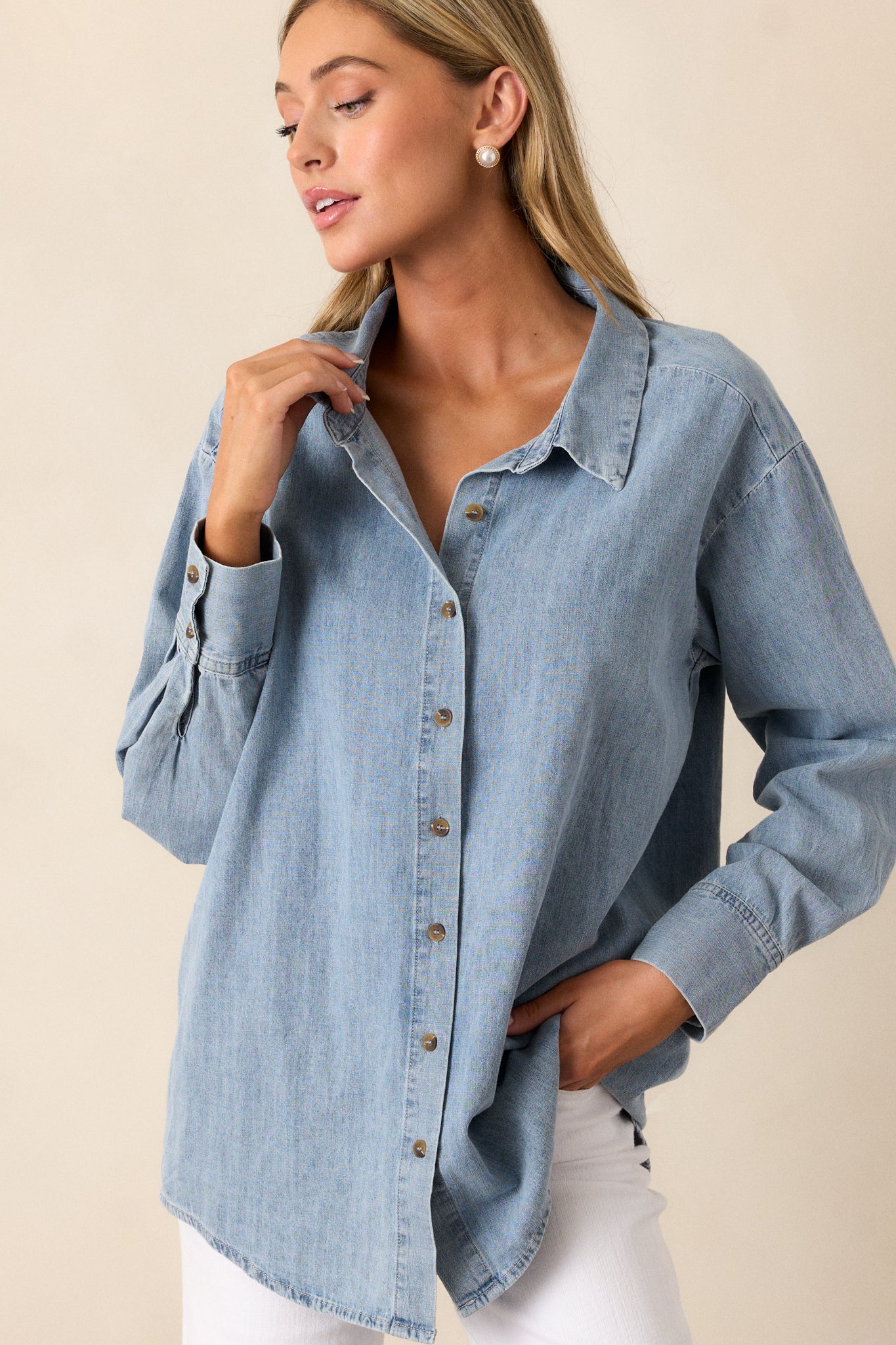 Front angled view of a chambray top featuring a collared neckline, functional buttons down the front, long sleeves with buttoned cuffs, and a scoop bottom hemline. 