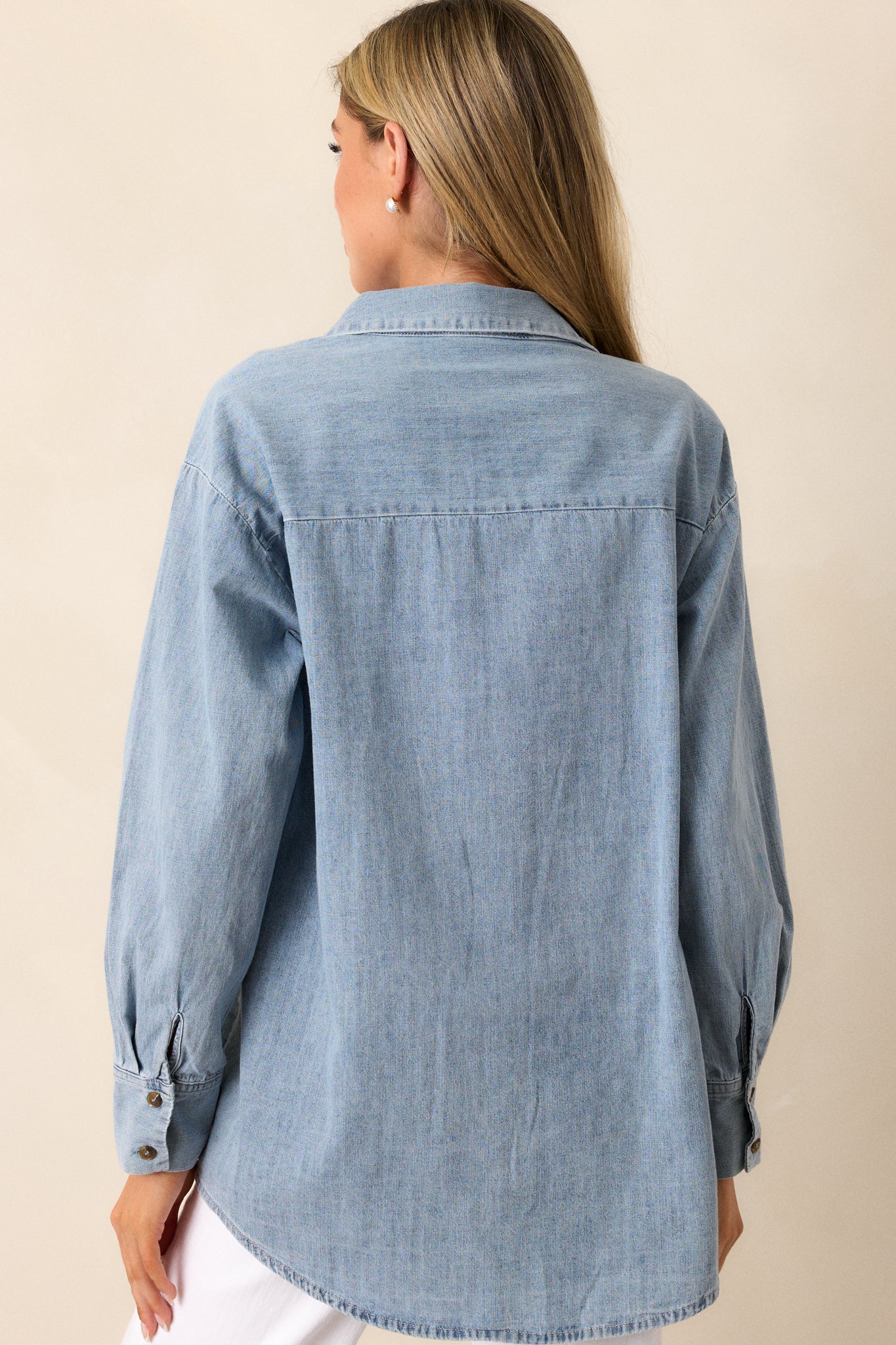 Back view of a chambray top highlighting the overall fit, long sleeves, and scoop bottom hemline.