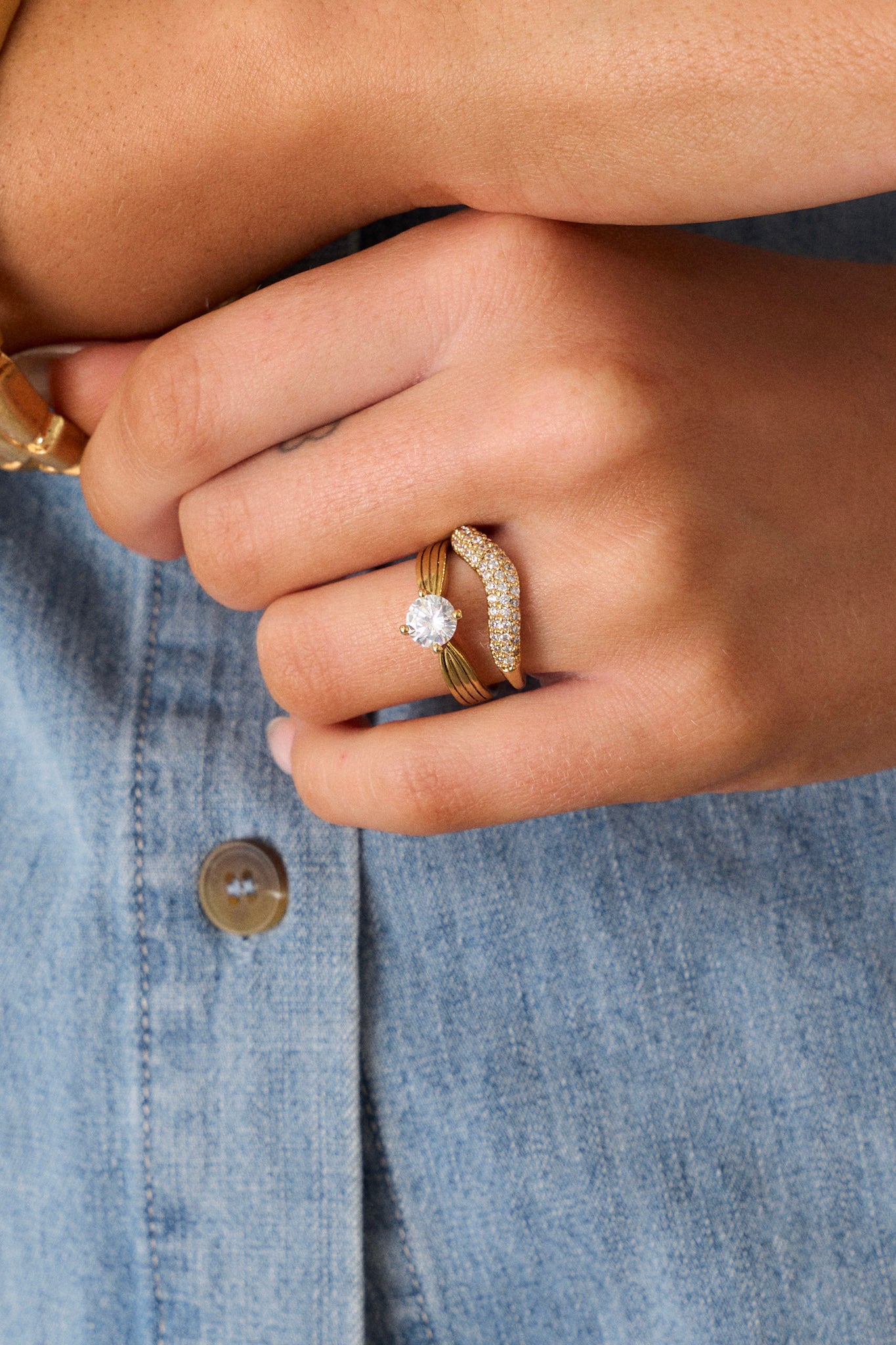 A pair of gold rings displayed together, featuring one ring with an arched middle decorated with tiny rhinestones and a solid textured band beside the second ring showcasing a diamond-shaped rhinestone set in the center of a slightly textured band.