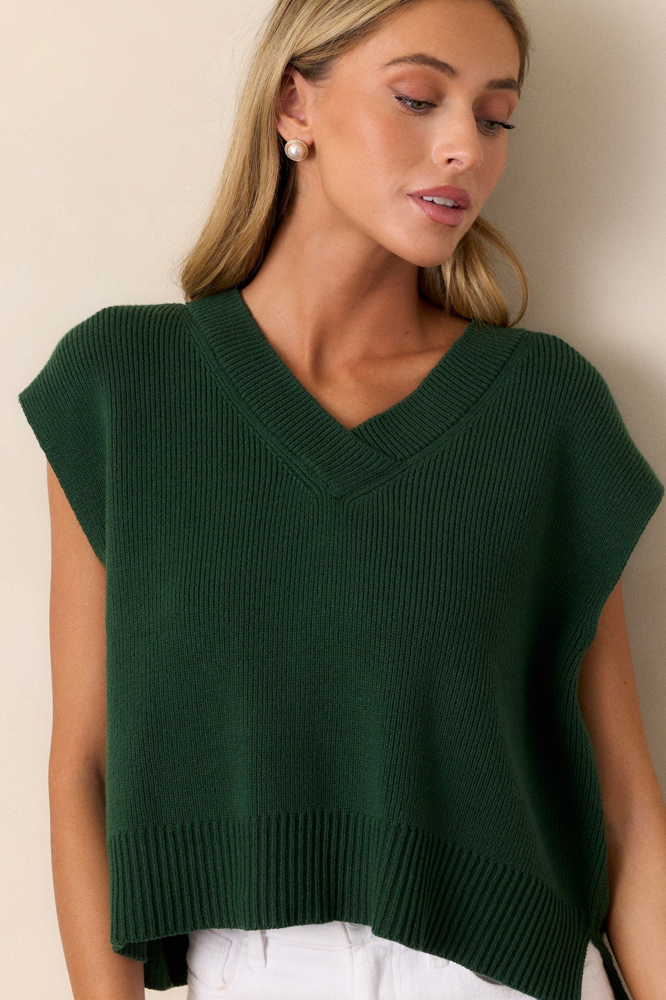 Close-up of a green sweater top highlighting the v-neckline and knit material with a thick hemline and short cap sleeves.