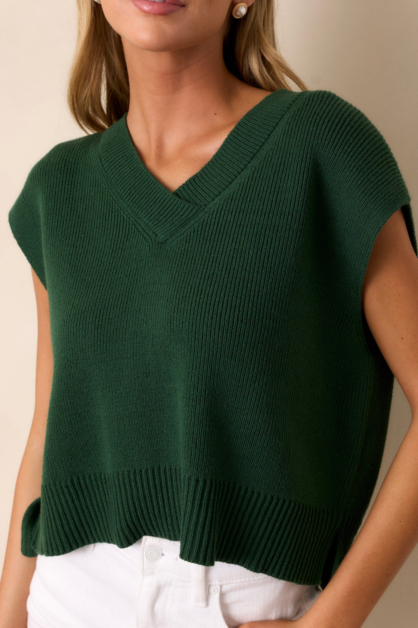 Close-up of the green sweater top's knit material, showcasing the thick hemline and side slits in the hem.