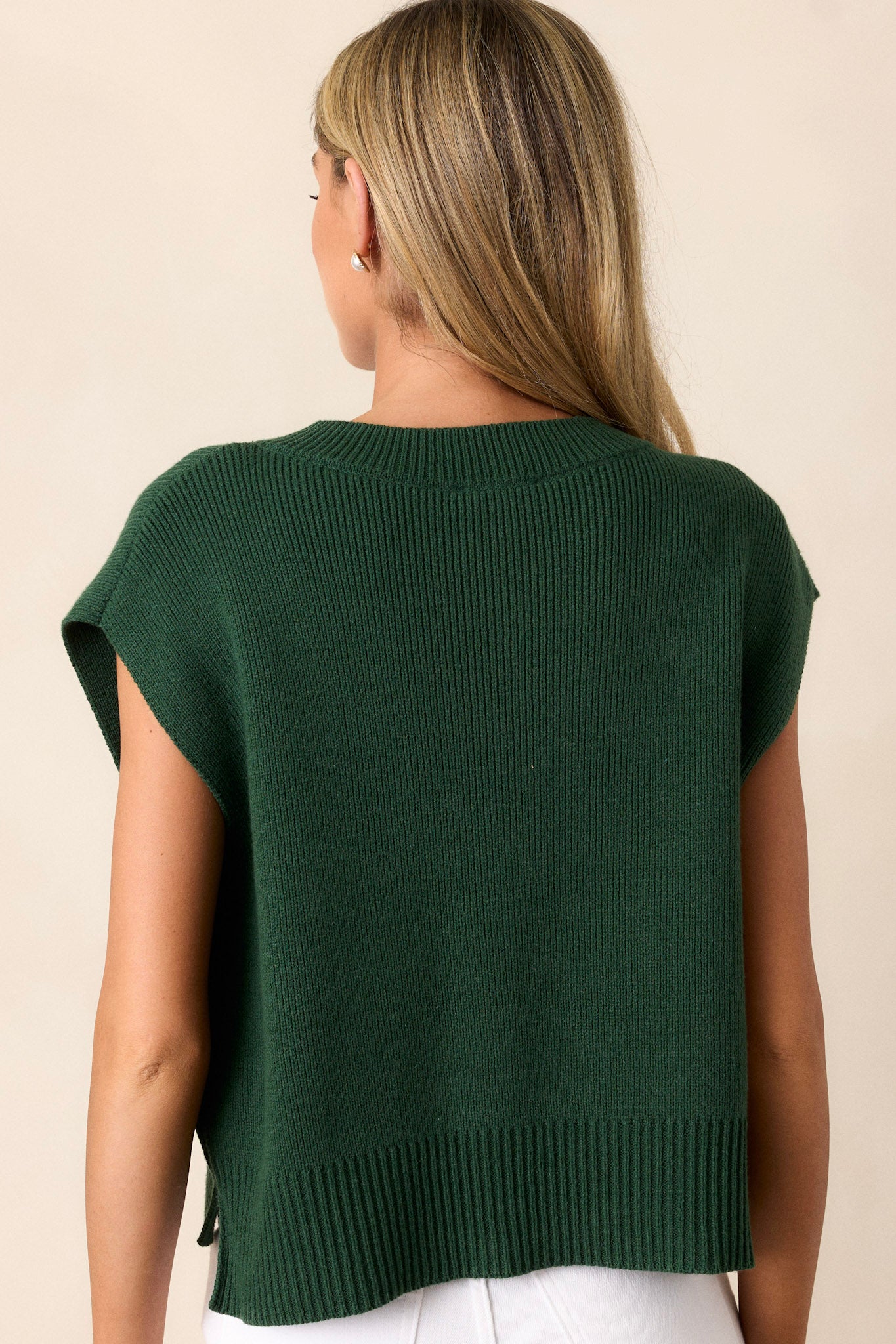 The back of the green sweater top displaying the knit material, thick hemline, and side slits in the hem.