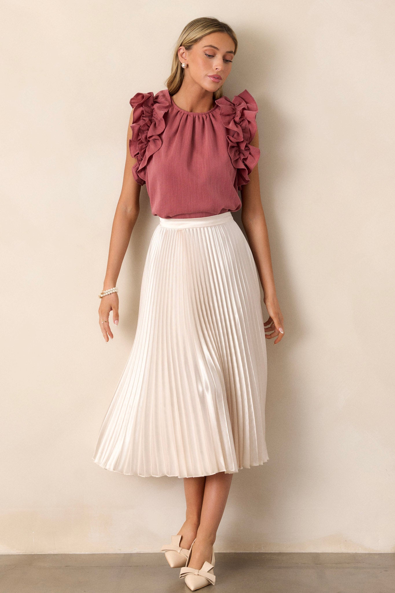 Full length view of a rose top with a high crew neckline, a keyhole with a button closure at the back of the neck, and ruffled shoulder detailing