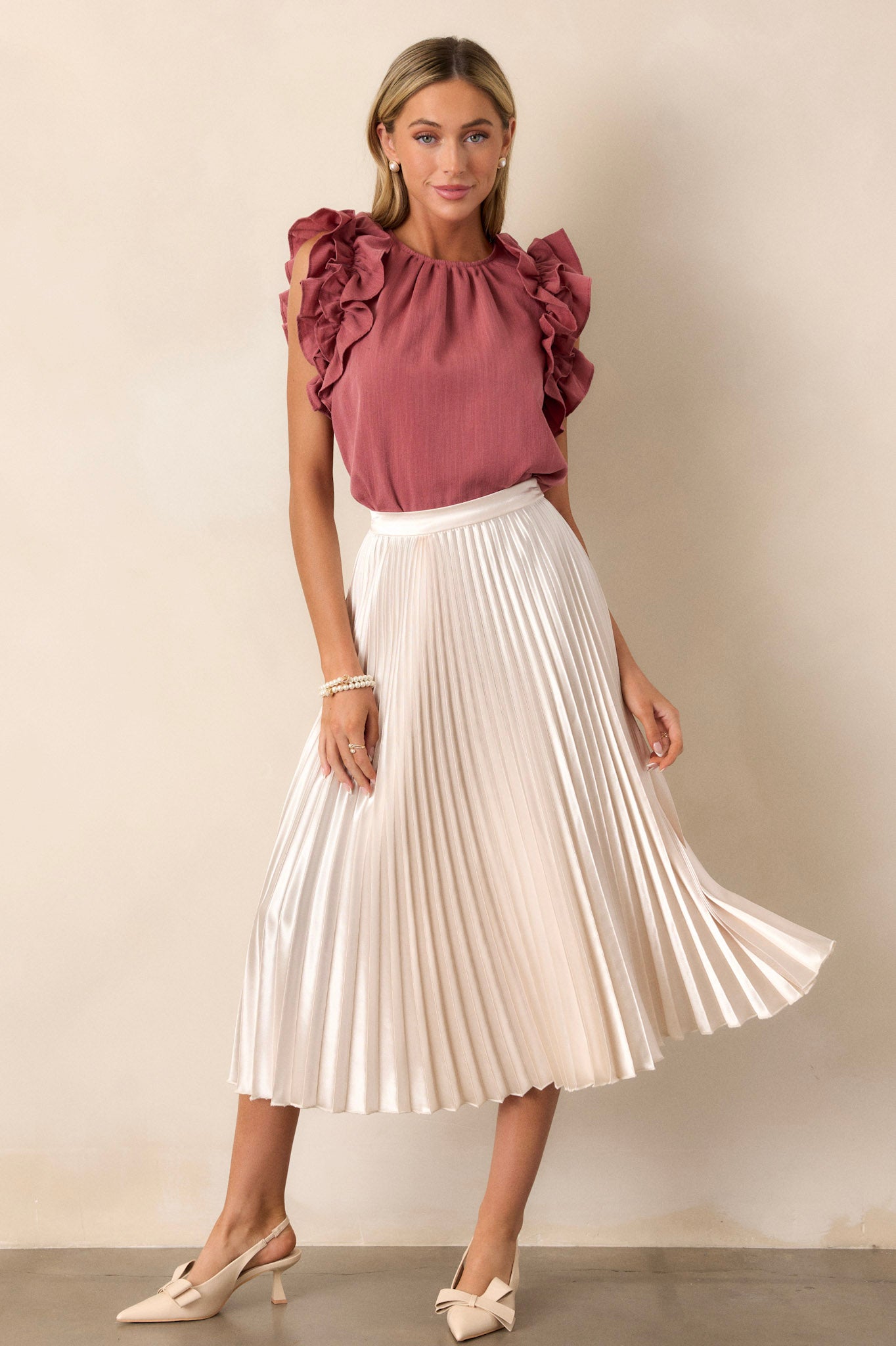 Action shot of a rose top displaying the fit and movement, highlighting the high crew neckline, ruffled shoulder detailing, and keyhole with a button closure at the back of the neck.