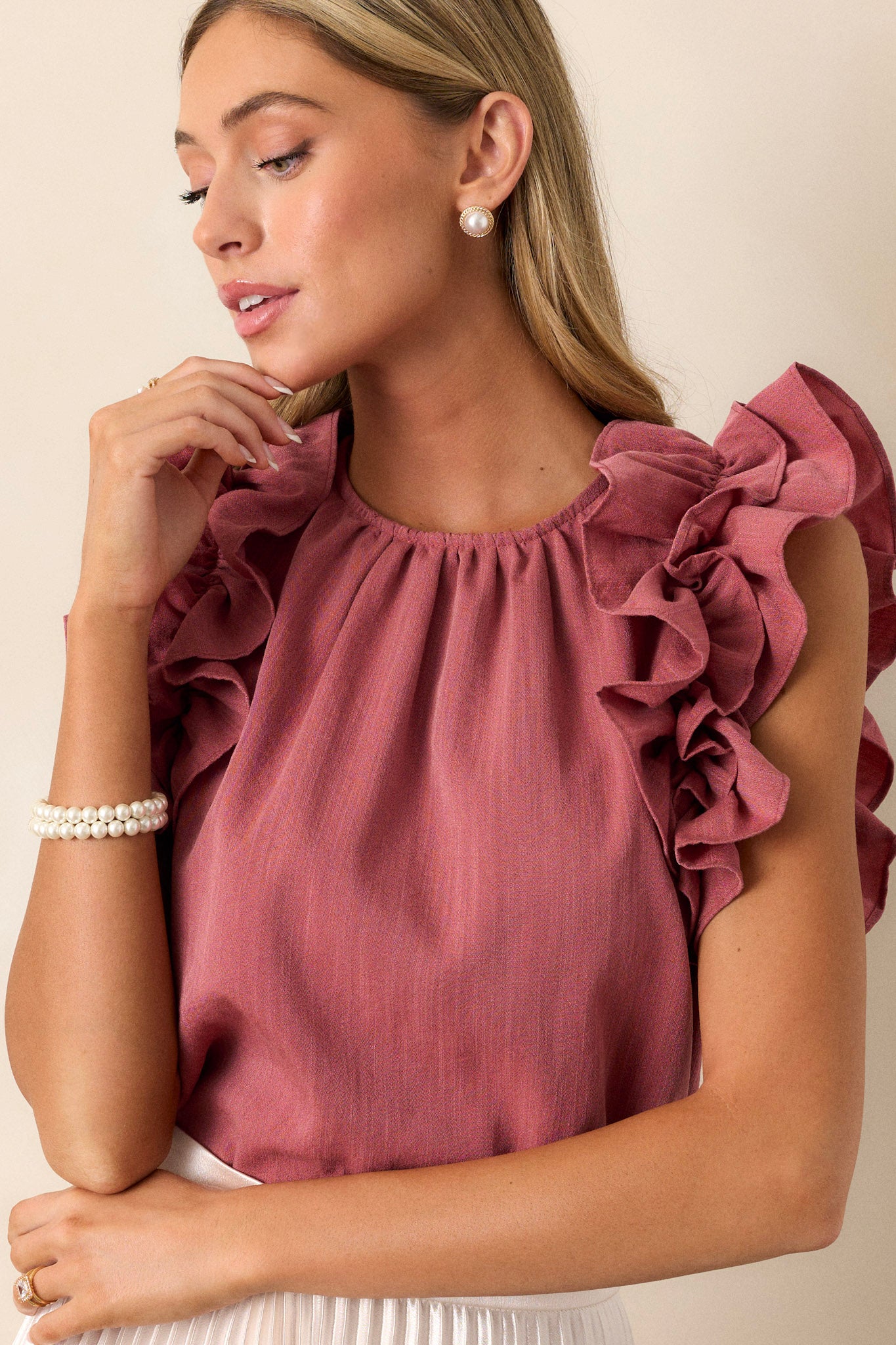 Front angled view of a rose top featuring a high crew neckline, a keyhole with a button closure at the back of the neck, and ruffled shoulder detailing