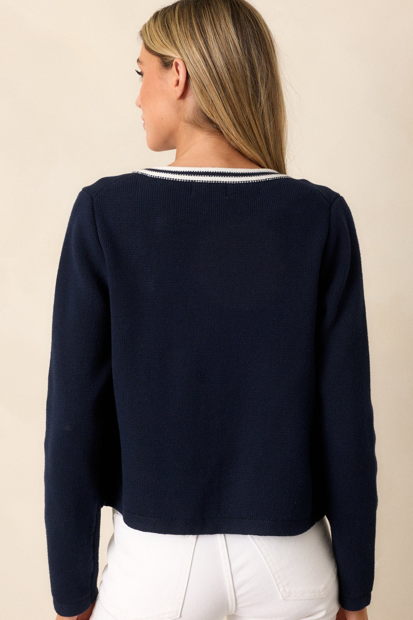 Back view of a navy knit cardigan highlighting the open knit pattern, striped detailing, and the overall structure of the long cuffed sleeves.