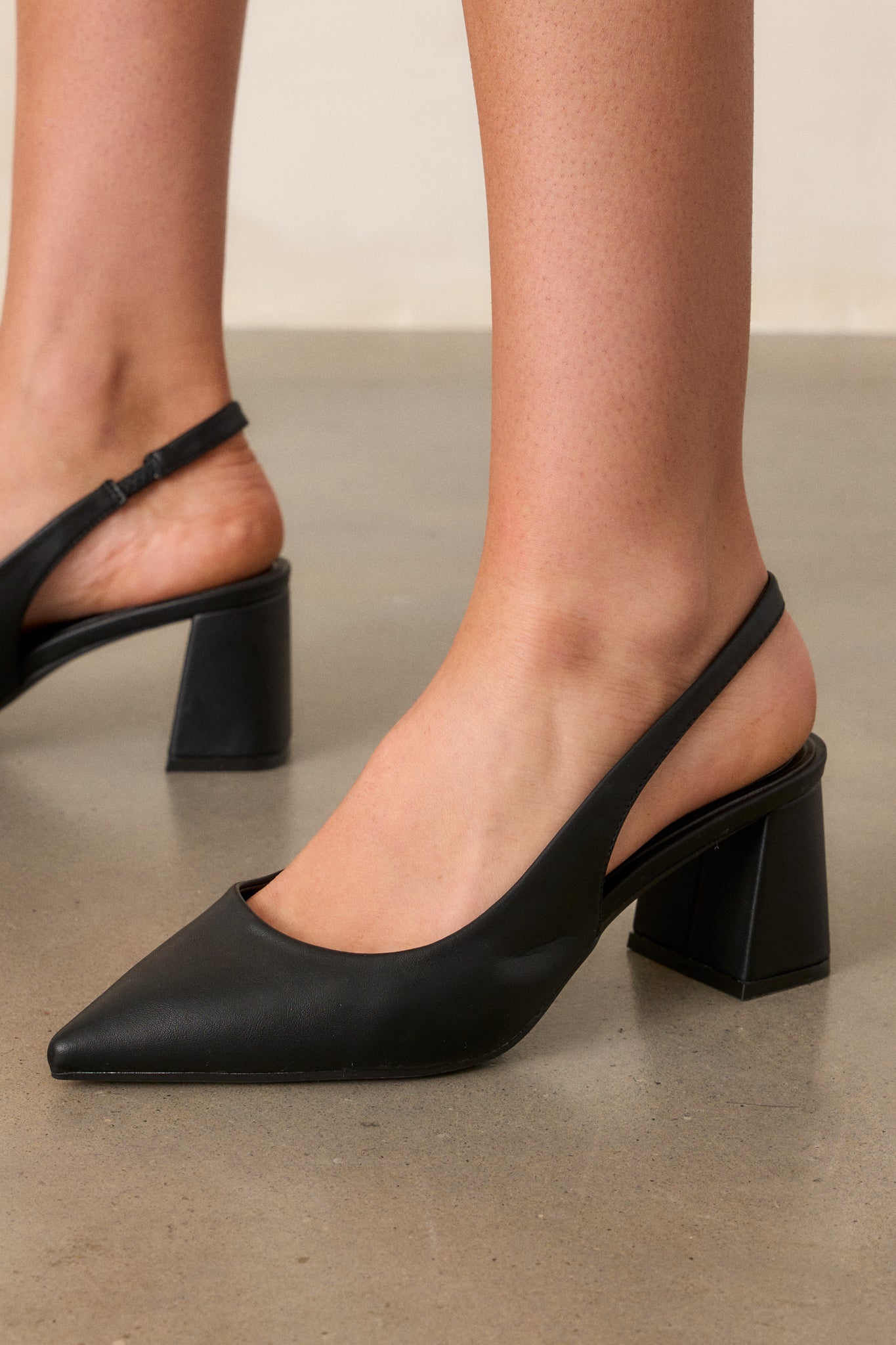 Extreme close-up of the faux leather material of the black heels, highlighting the texture and finish around the pointed toe.