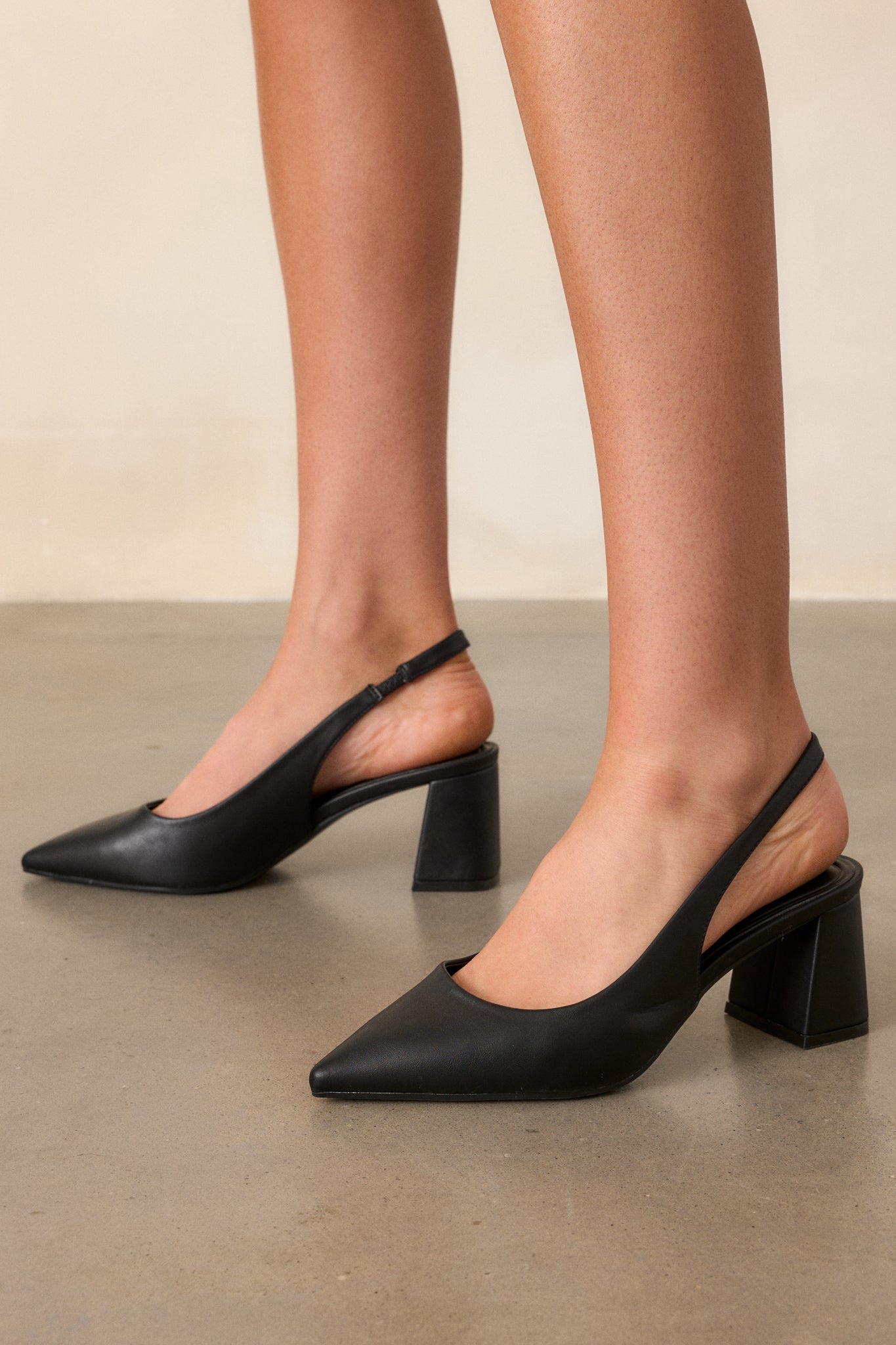 Close-up of black heels featuring a pointed toe and a thick block heel, highlighting the smooth faux leather material.