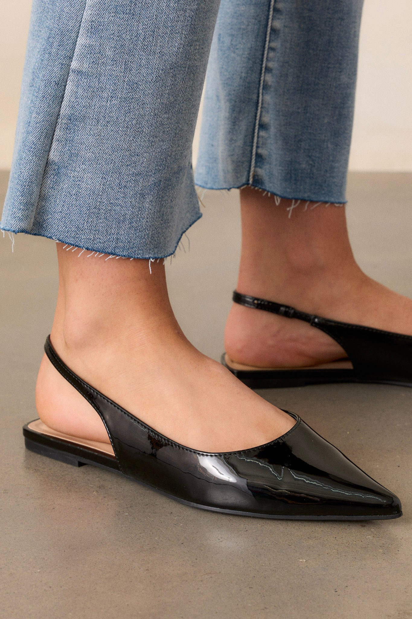 Close-up detail of the slingback strap and patent finish, highlighting the texture and shine of the black flats.