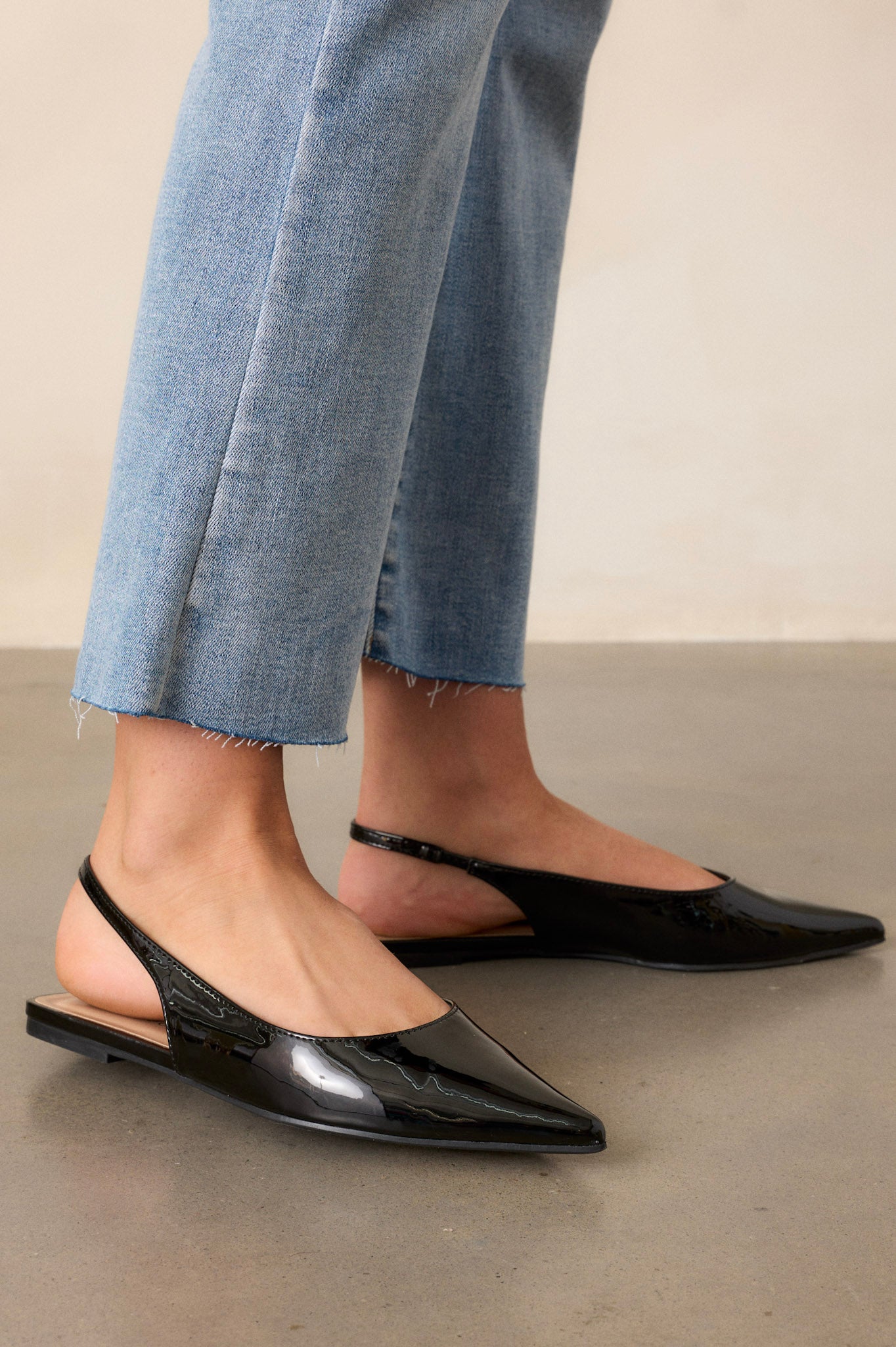 Side view of black flats, emphasizing the pointed toe and the slim slingback-style strap with a shiny patent finish.