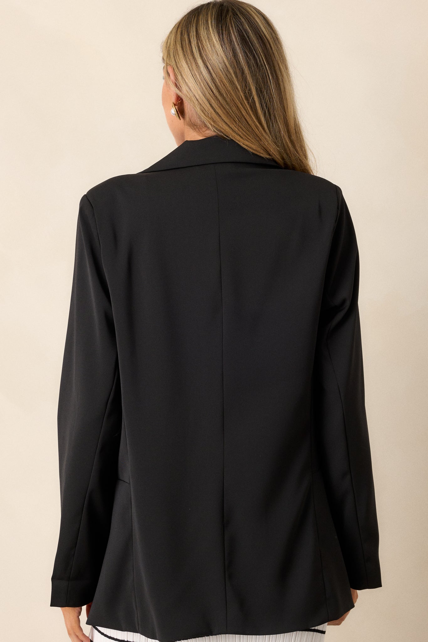 A back view of the black blazer, highlighting the smooth back design, tailoring details, and lightweight shoulder pads.