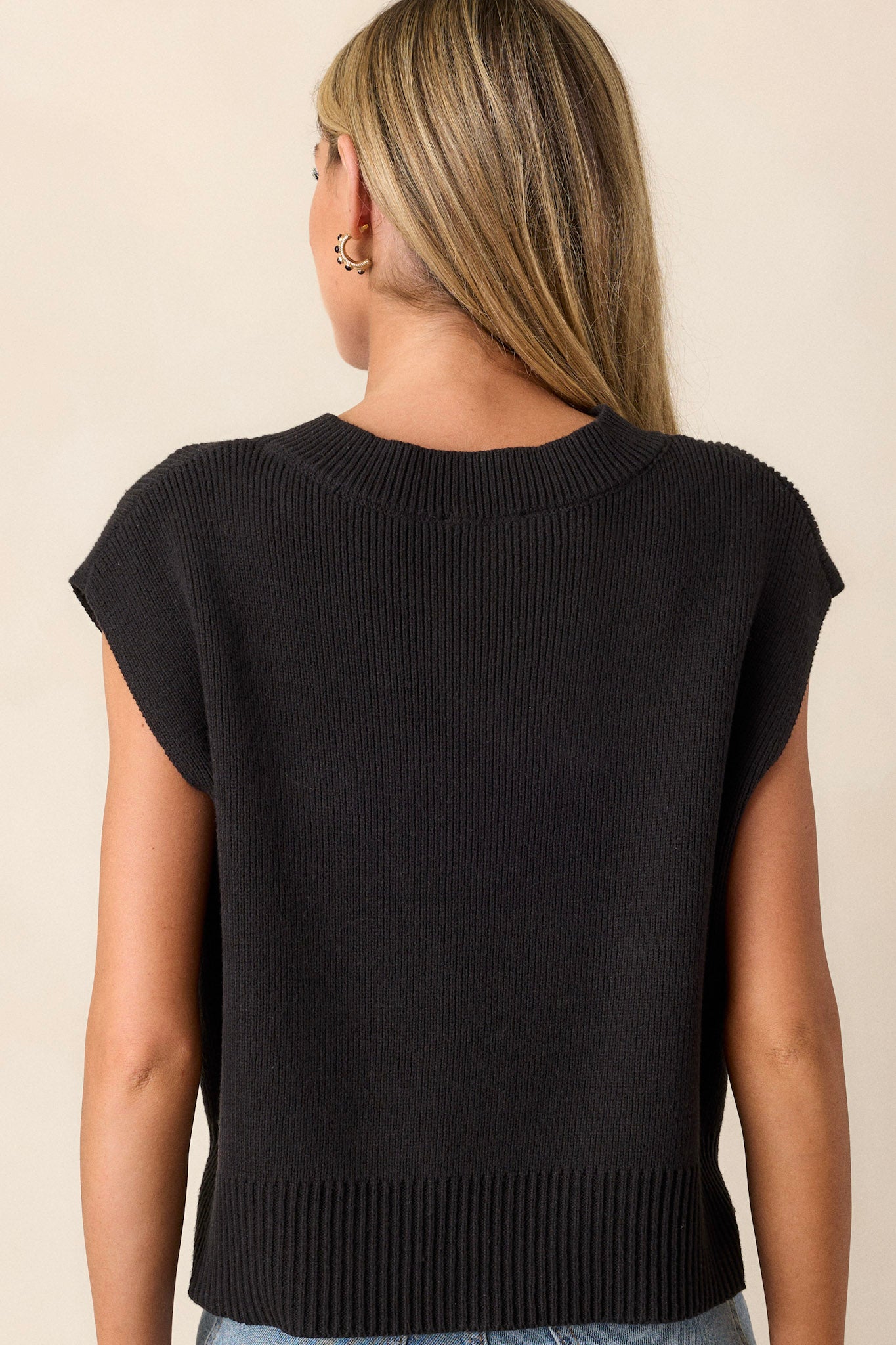 Back view of a black sweater top highlighting the overall fit, thick hemline, side slits in the hem, and short sleeves.