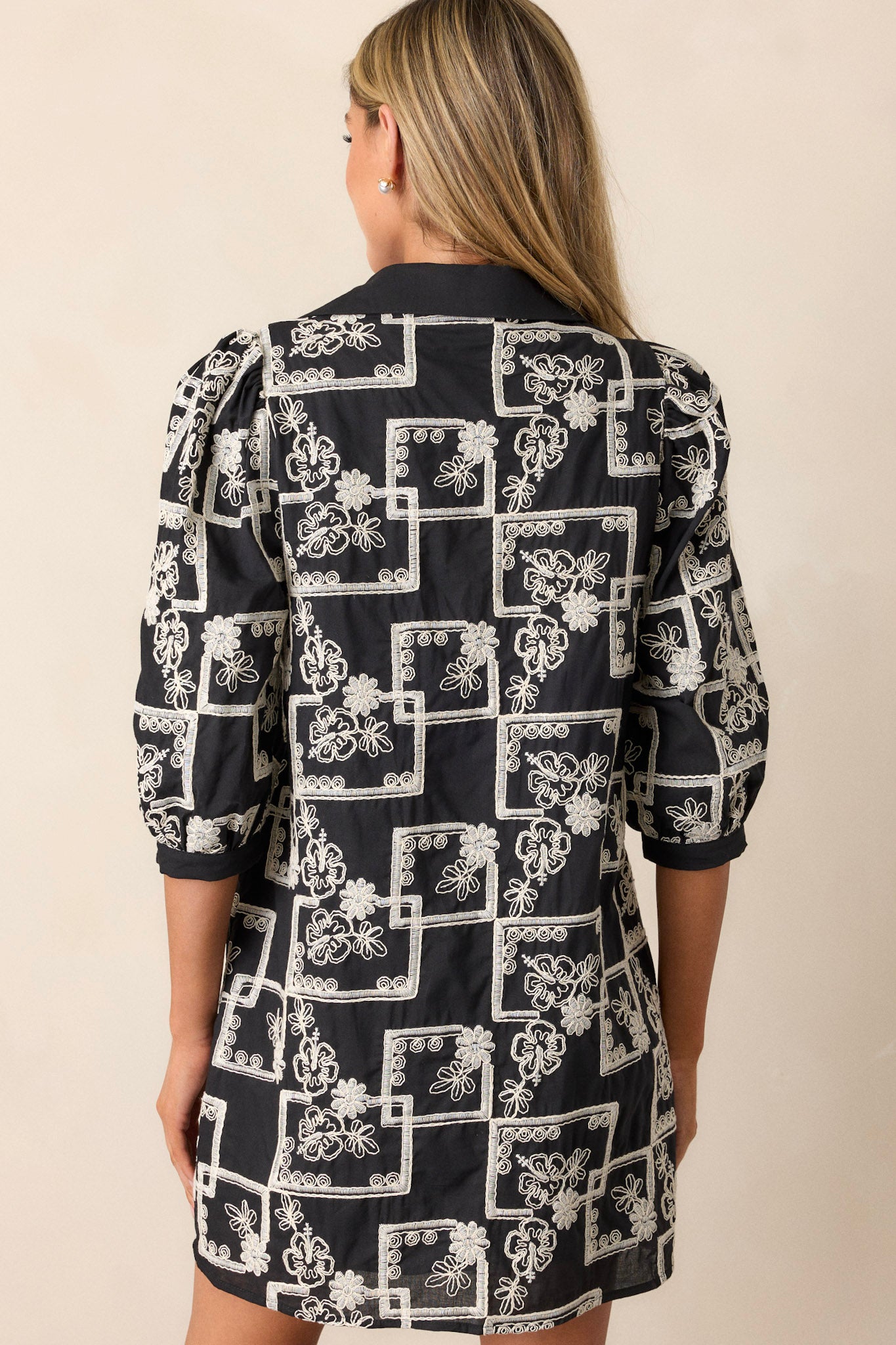 Back view of this dress that features a collared neckline, a functional button up bust, a white embroidered floral and square pattern, a relaxed fit and puffed half sleeves.