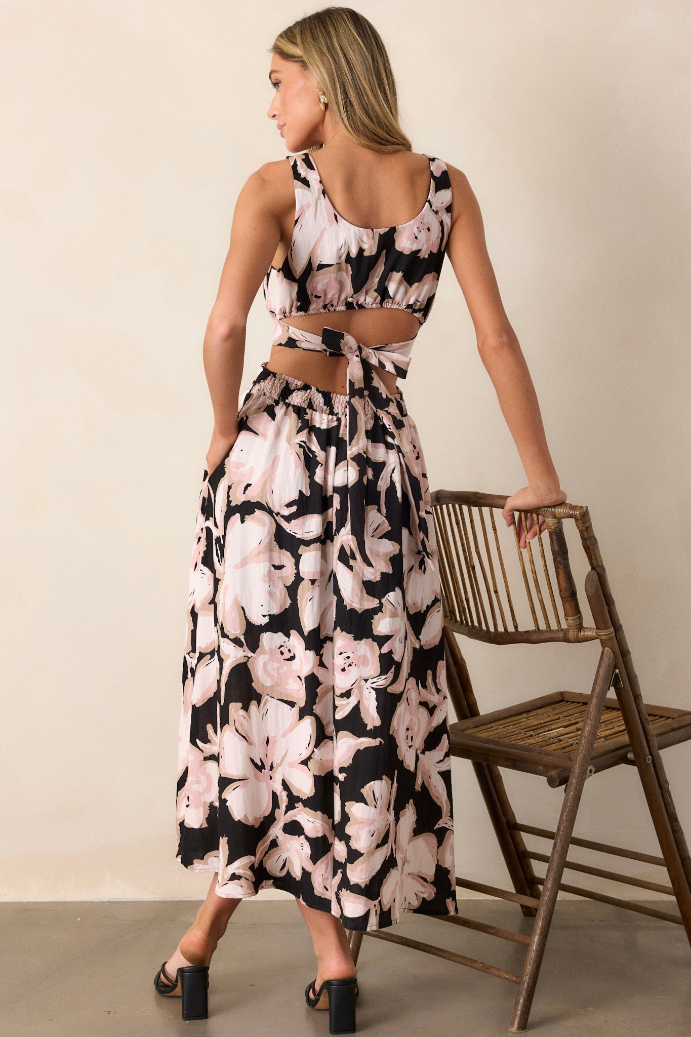 Back view of this black maxi dress that features a square neckline, thick straps, an elastic back insert, a self-tie back feature, waist cutouts with a smocked back insert, functional hip pockets, and an all over floral pattern.