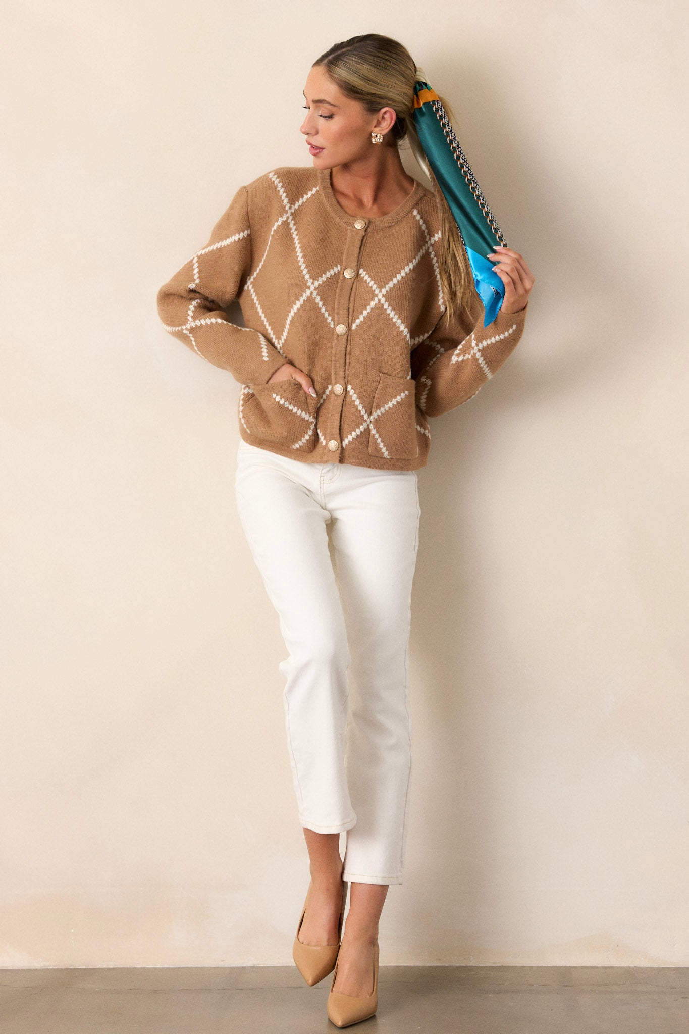 A full-length view of the tan sweater, highlighting the simple tan and white knit argyle pattern and the rounded neckline.