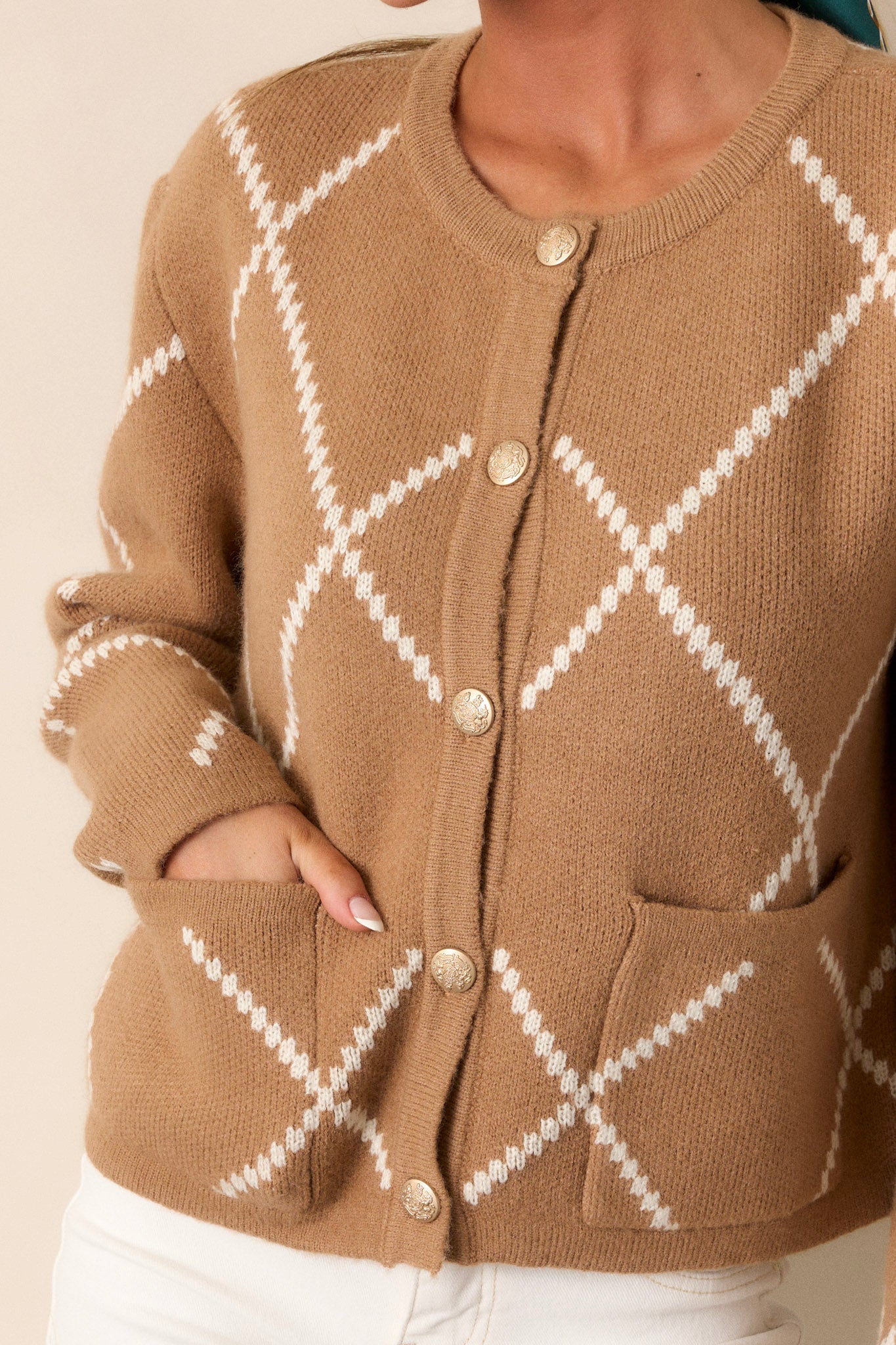 A close-up image of the button detailing, showcasing the gold embellishment and the texture of the knit fabric surrounding it.