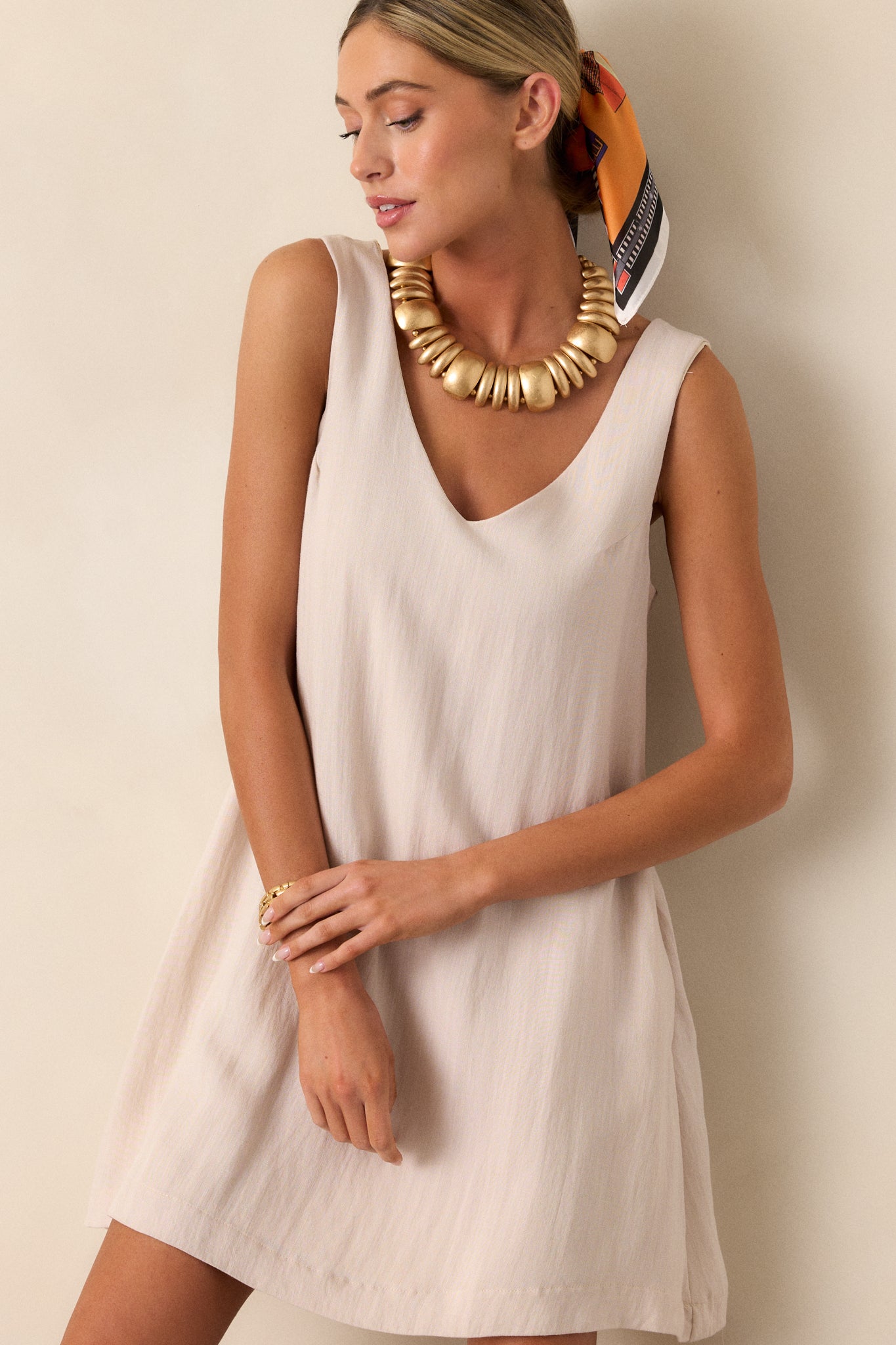 Front view of an ivory mini dress featuring a v-neckline, a sleeveless design, two functional hip pockets, and a shift silhouette.