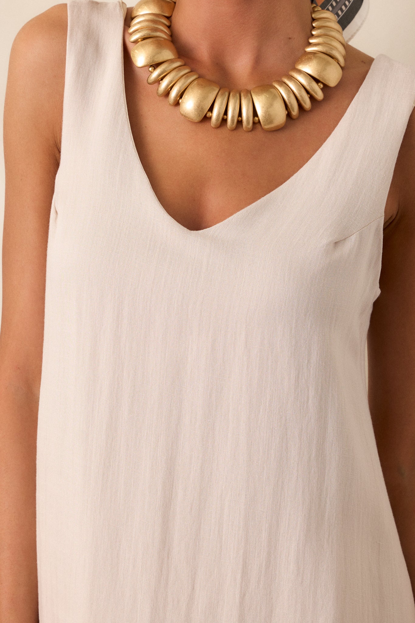 Close up on the v-neckline of this ivory, sleeveless shift dress. 