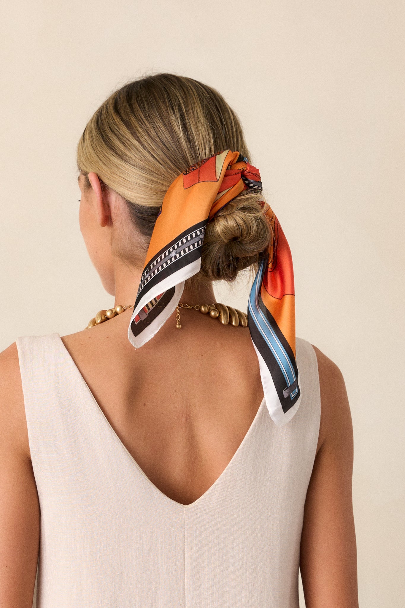 An orange multi print satin scarf styled in models hair. 