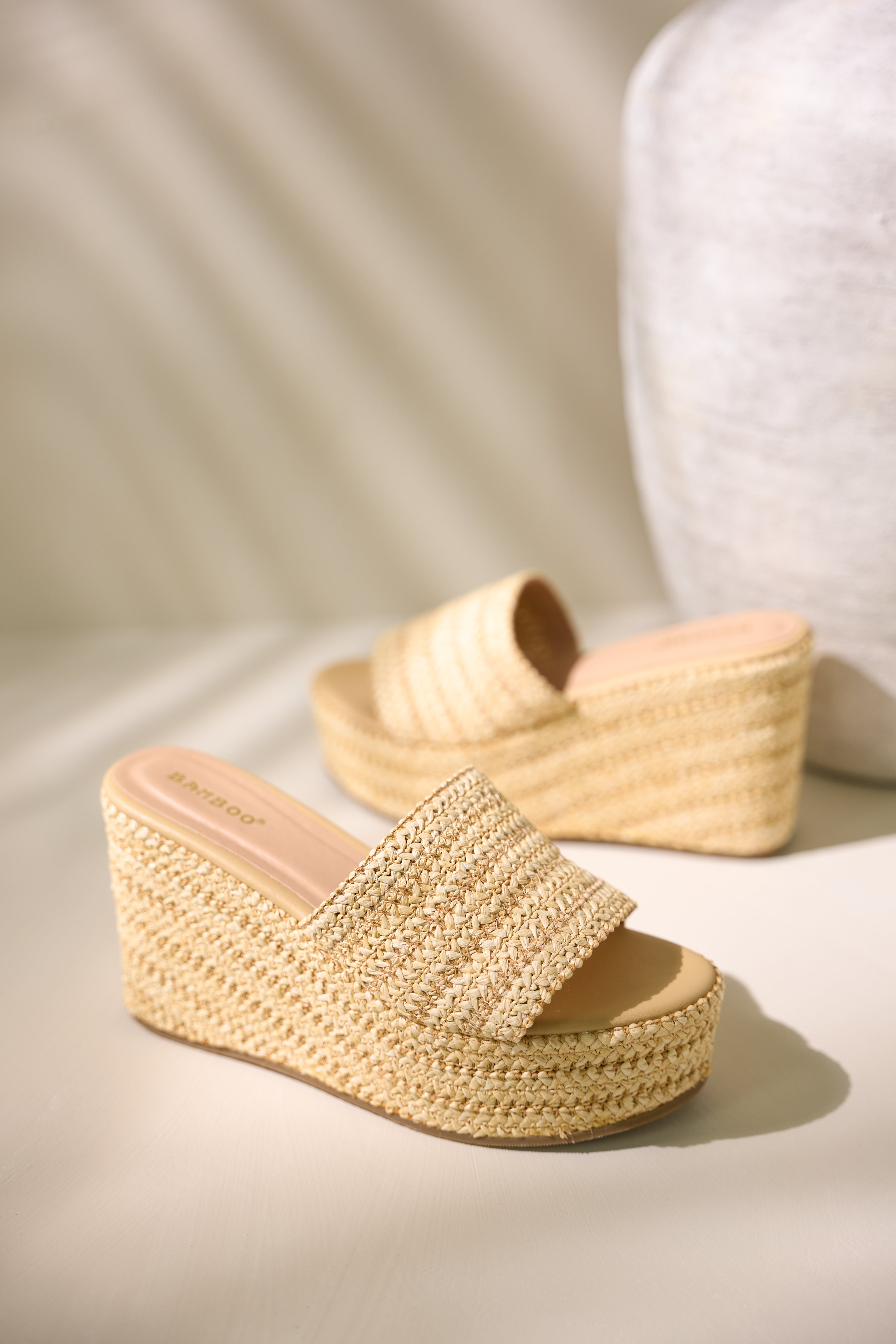 These natural sandals feature a rounded toe, slide on style, a raffia material, and a platform design.