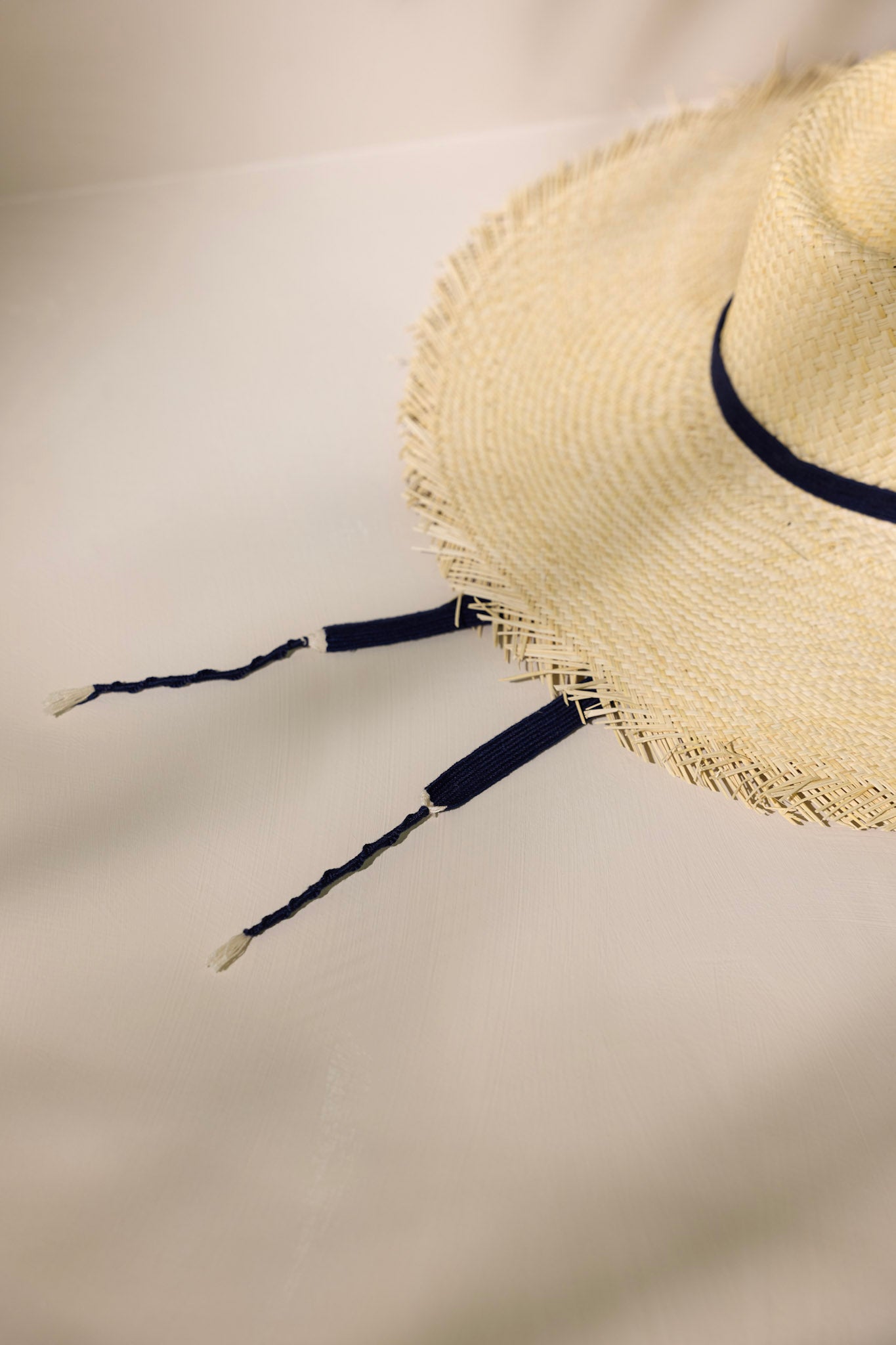 Detail shot of this Miriam hat features features a cotton navy band with a self-tie feature, and a fringed wide brim.