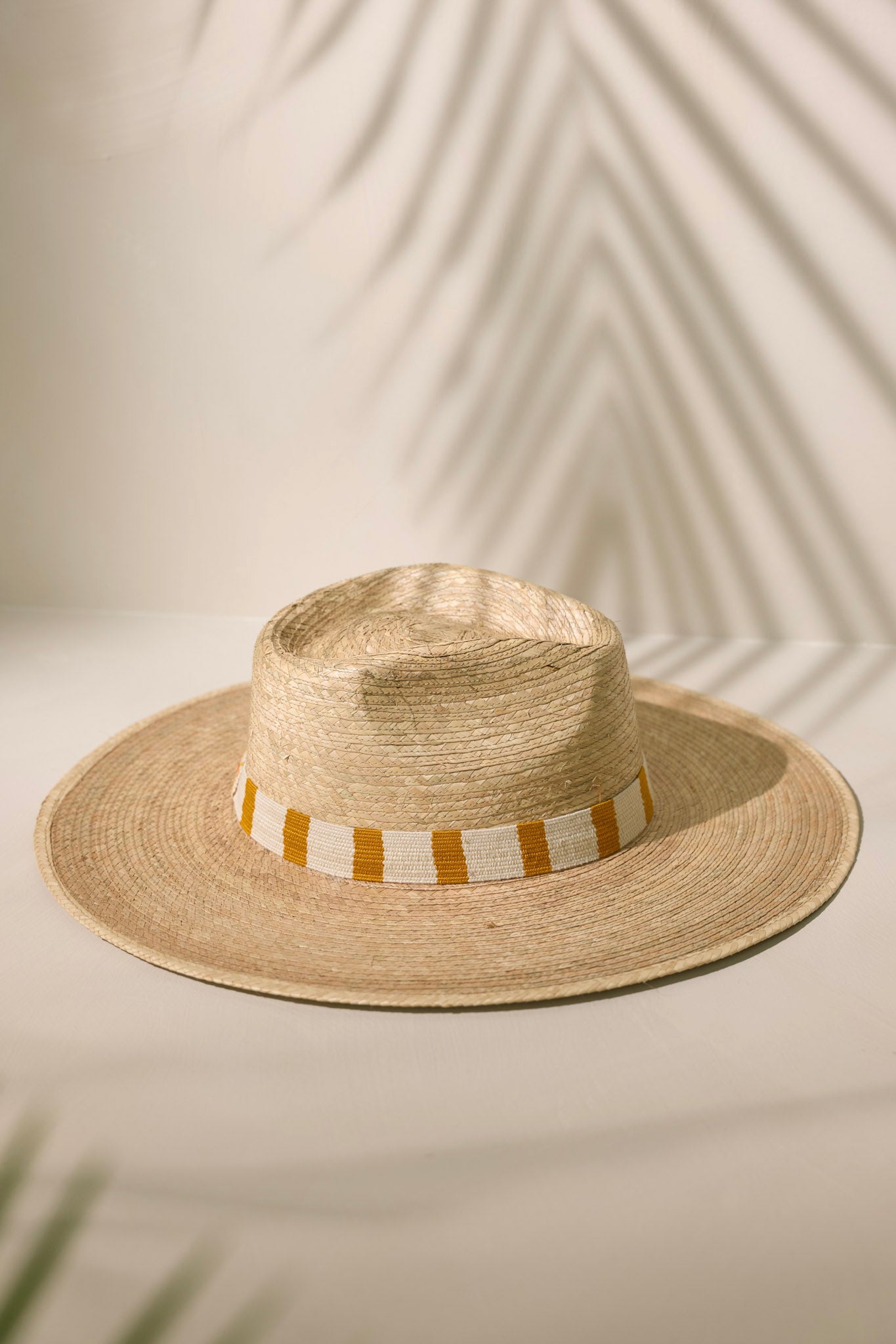 Overhead view of this Carmen Palm Hat featuring a cotton woven band with mustard yellow and white stripes, and is handmade with palm fronds.