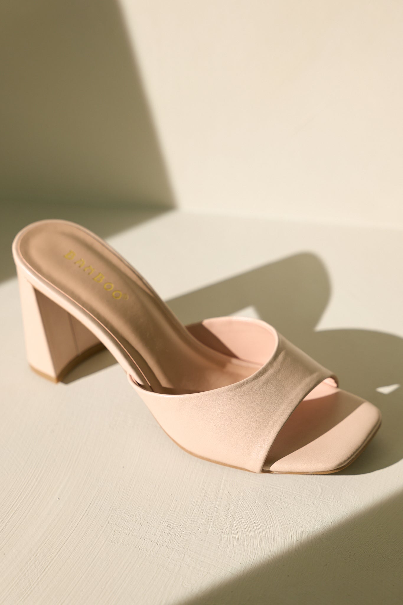 Top view of these beige heels that feature a square toe, a slip-on design, a strap over the top of the foot, and a thick block heel.