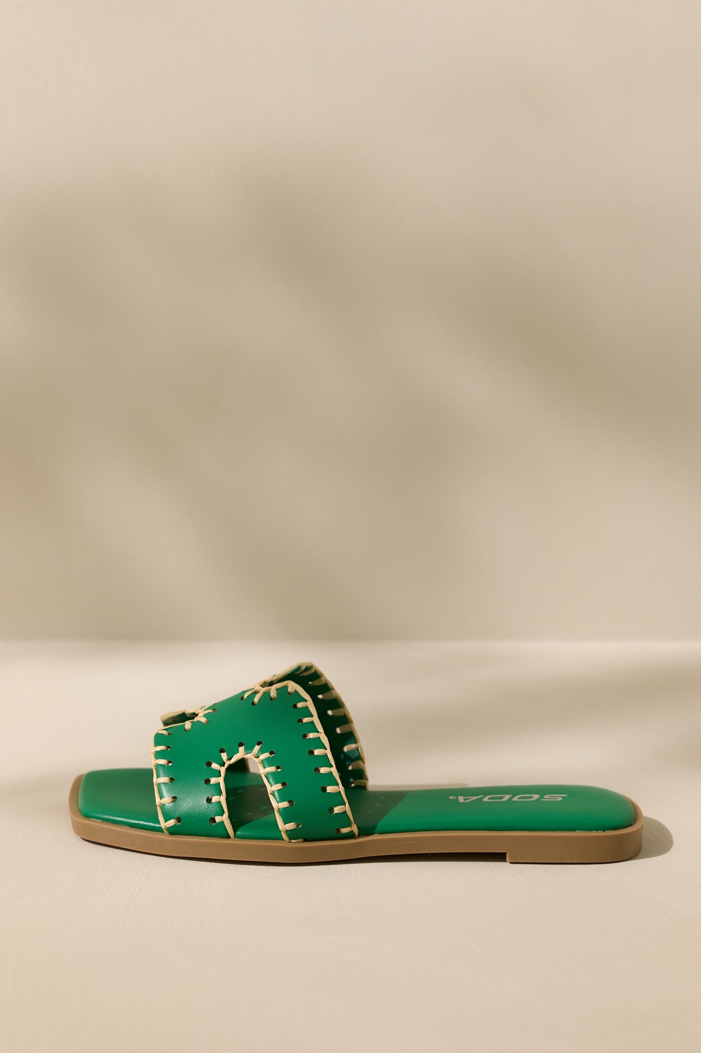 Side view of these green sandals that feature a square toe, a slip on design, a strap with cutouts over the top of the foot beige stitch detailing, and a high contrasting sole.