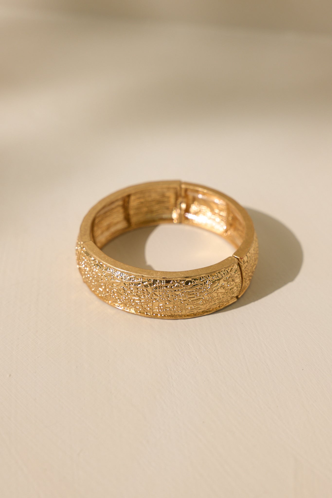 Stand alone view of this gold bracelet that features a heavily textured material, and elastic bands underneath to accommodate stretch.